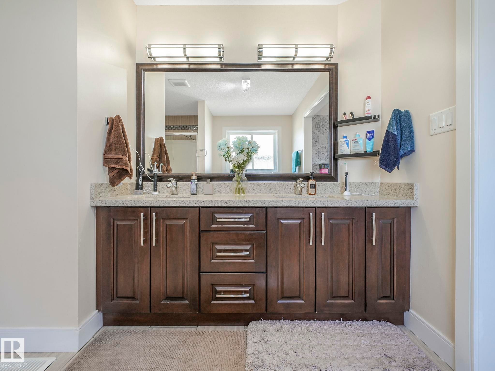 Double vanity featuring dark wood cabinetry with brushed nickel hardware, stone-finish countertop, and undermount sinks - 3910 49 Avenue, Beaumont, AB - Indoor Photo Showing Bathroom
