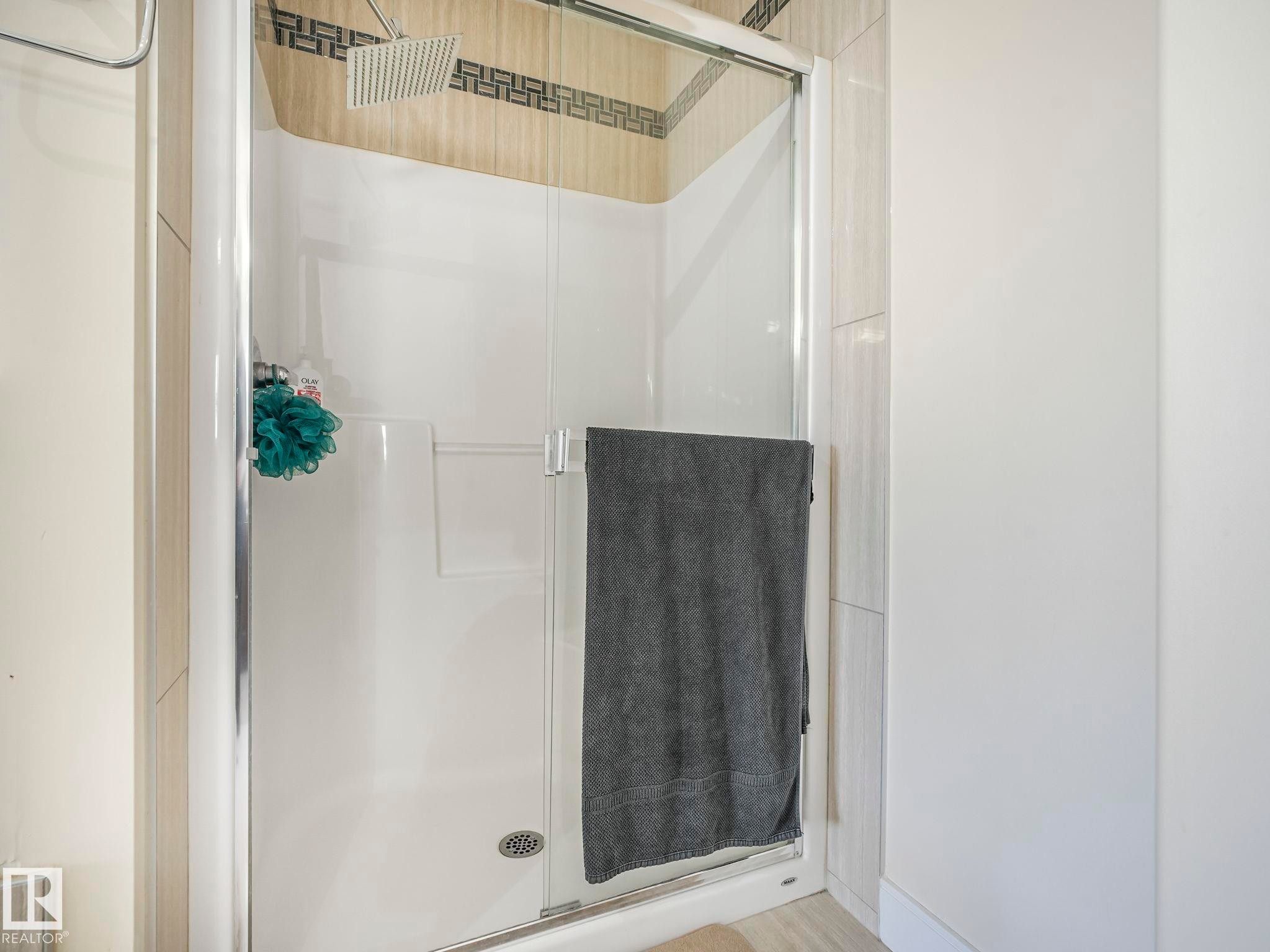 Enclosed shower stall featuring a rainfall showerhead, glass door, and decorative tile accent band - 3910 49 Avenue, Beaumont, AB - Indoor Photo Showing Bathroom