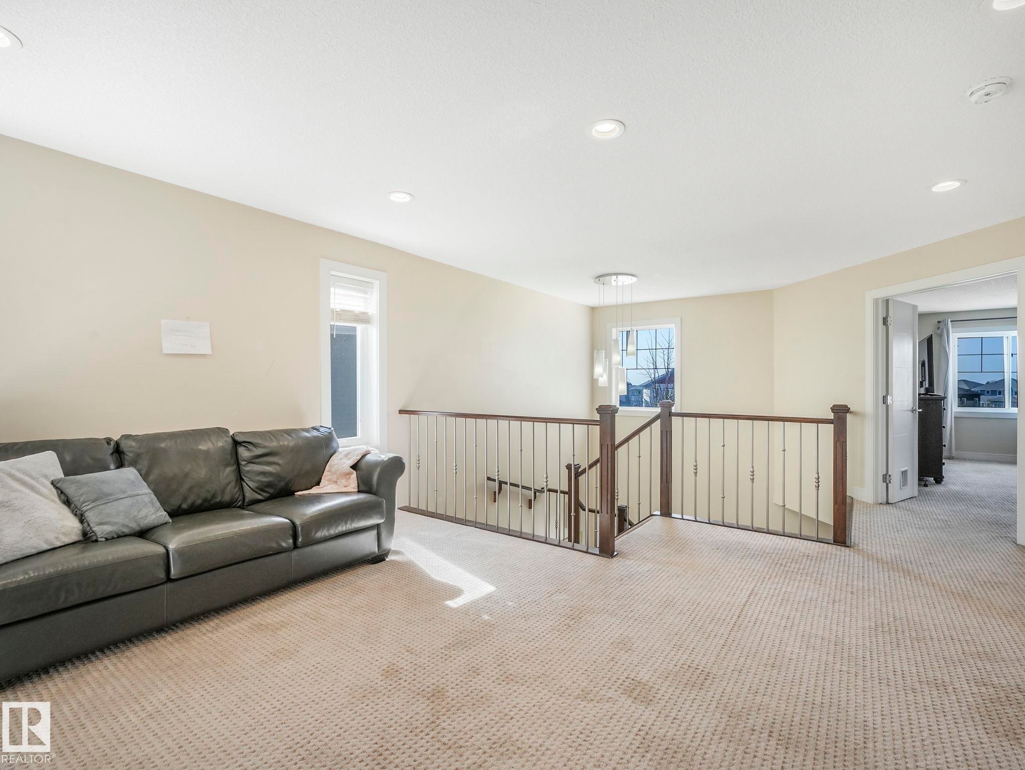 Carpeted loft space featuring recessed lighting, a contemporary chandelier, and a wood and metal baluster railing - 3910 49 Avenue, Beaumont, AB - Indoor