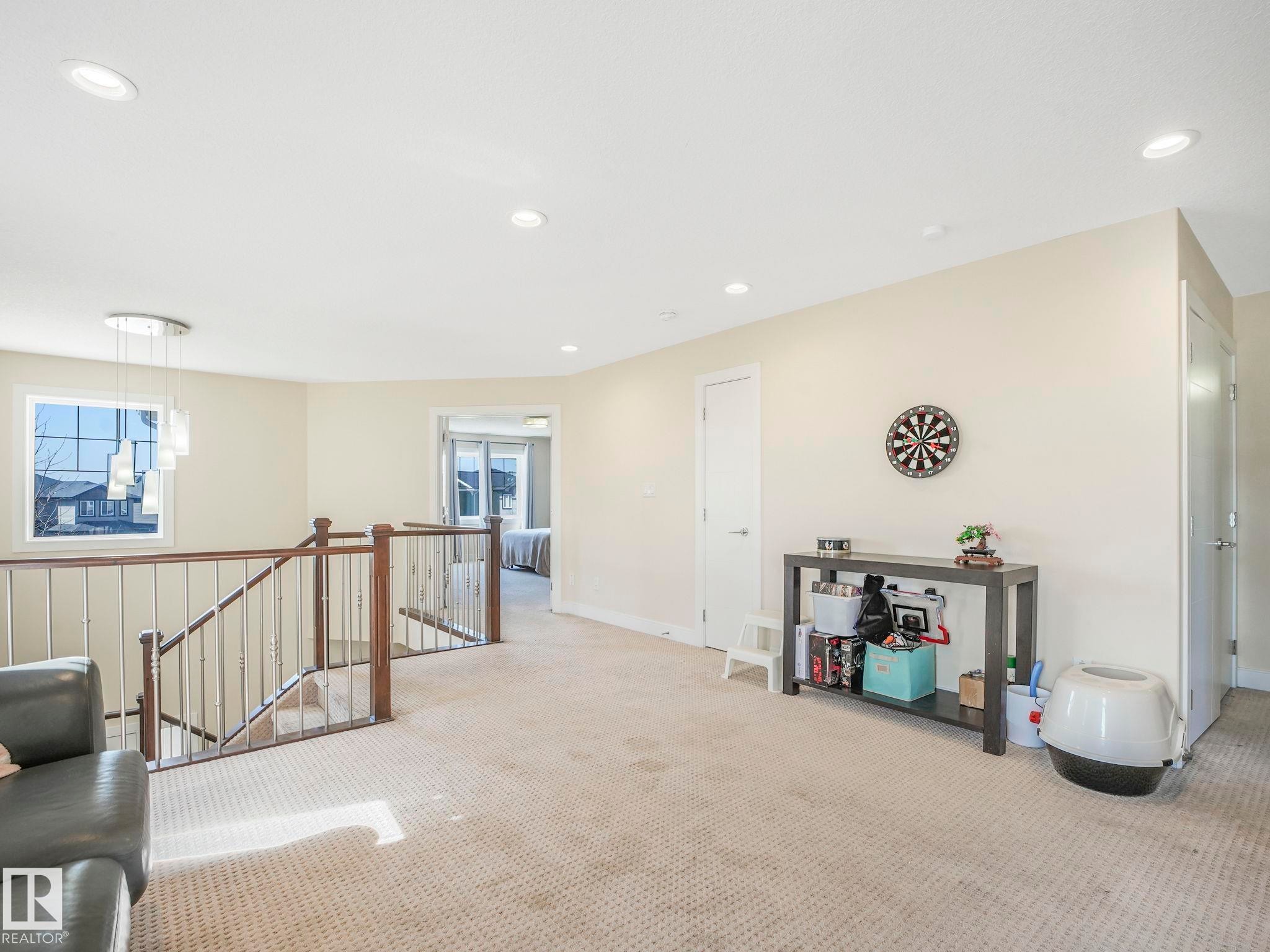 Carpeted upper-level landing featuring a staircase with wood newel posts and metal balusters - 3910 49 Avenue, Beaumont, AB - Indoor Photo Showing Other Room