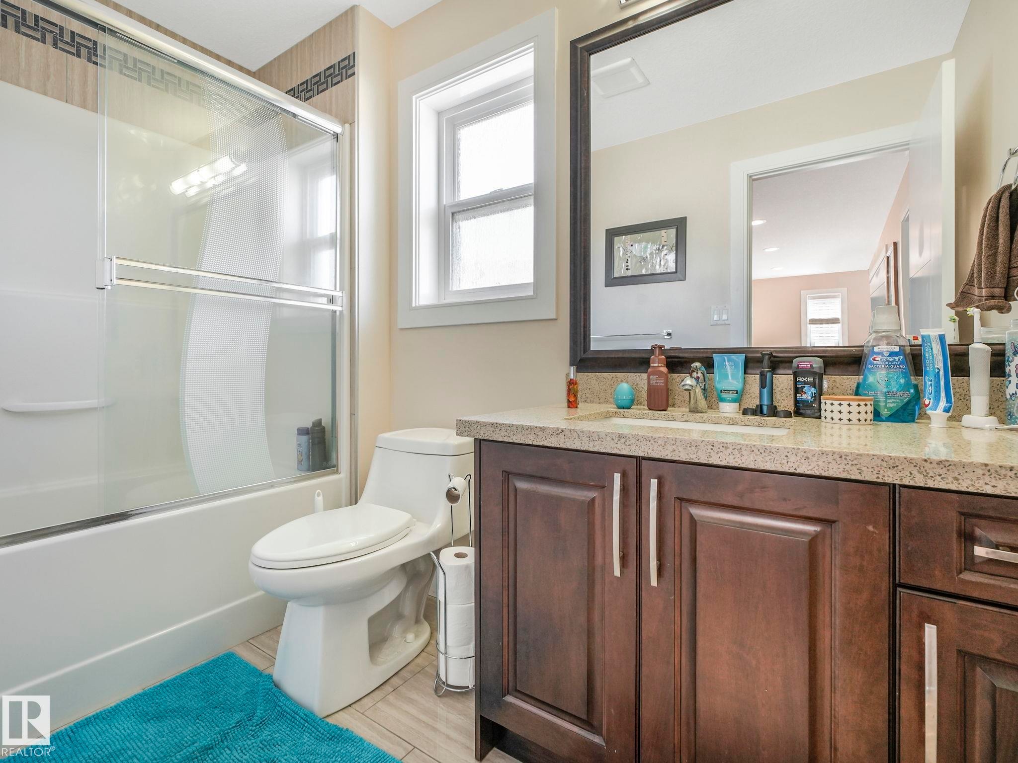 Bathroom featuring a dark wood-finish vanity with a light-toned countertop, a frameless mirror, and an integrated tub-shower combination with sliding glass doors - 3910 49 Avenue, Beaumont, AB - Indoor Photo Showing Bathroom