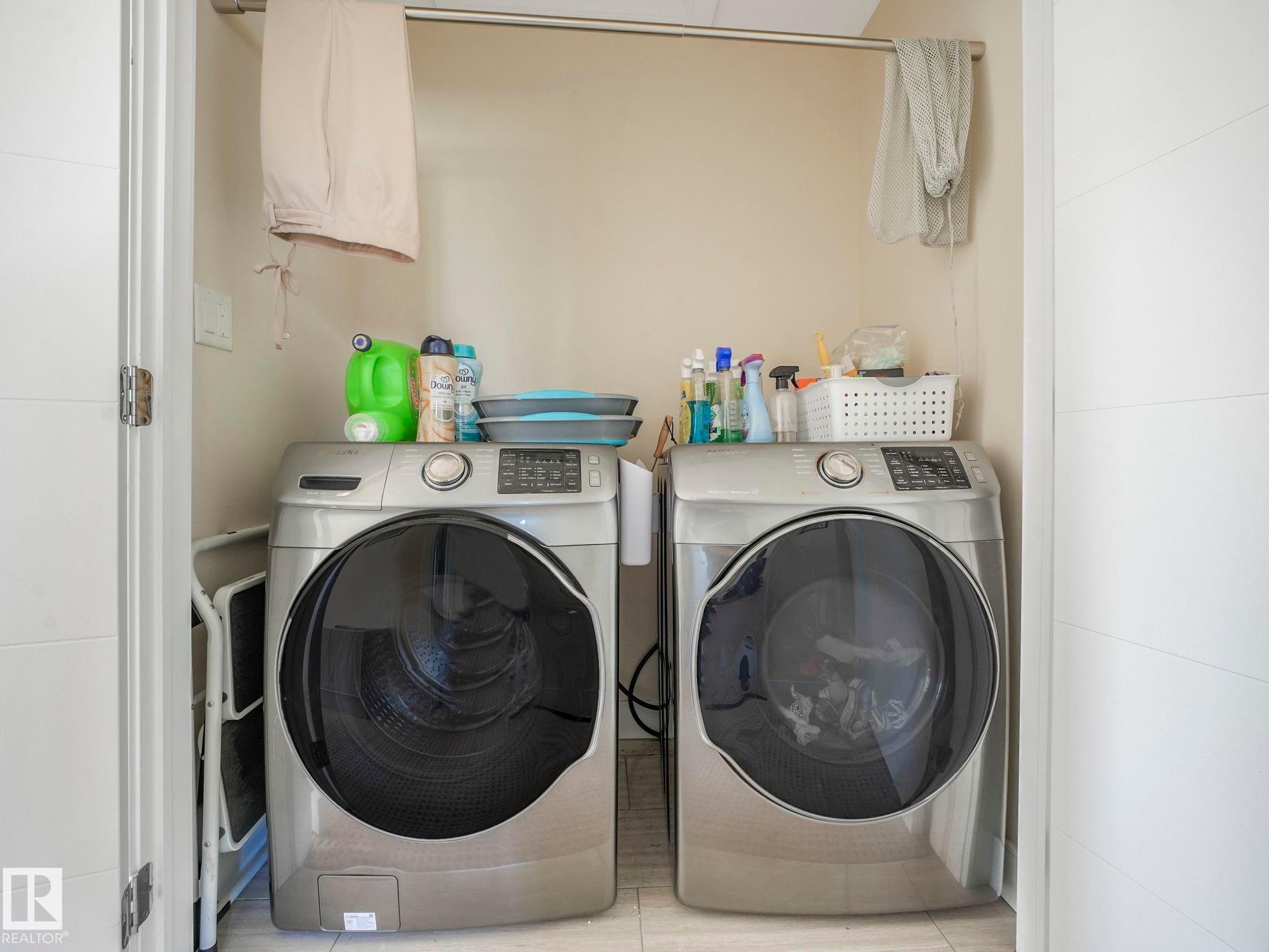 Dedicated laundry alcove featuring a front-loading washer and dryer set, a suspended clothes rod, and light-toned wall finishes - 3910 49 Avenue, Beaumont, AB - Indoor Photo Showing Laundry Room