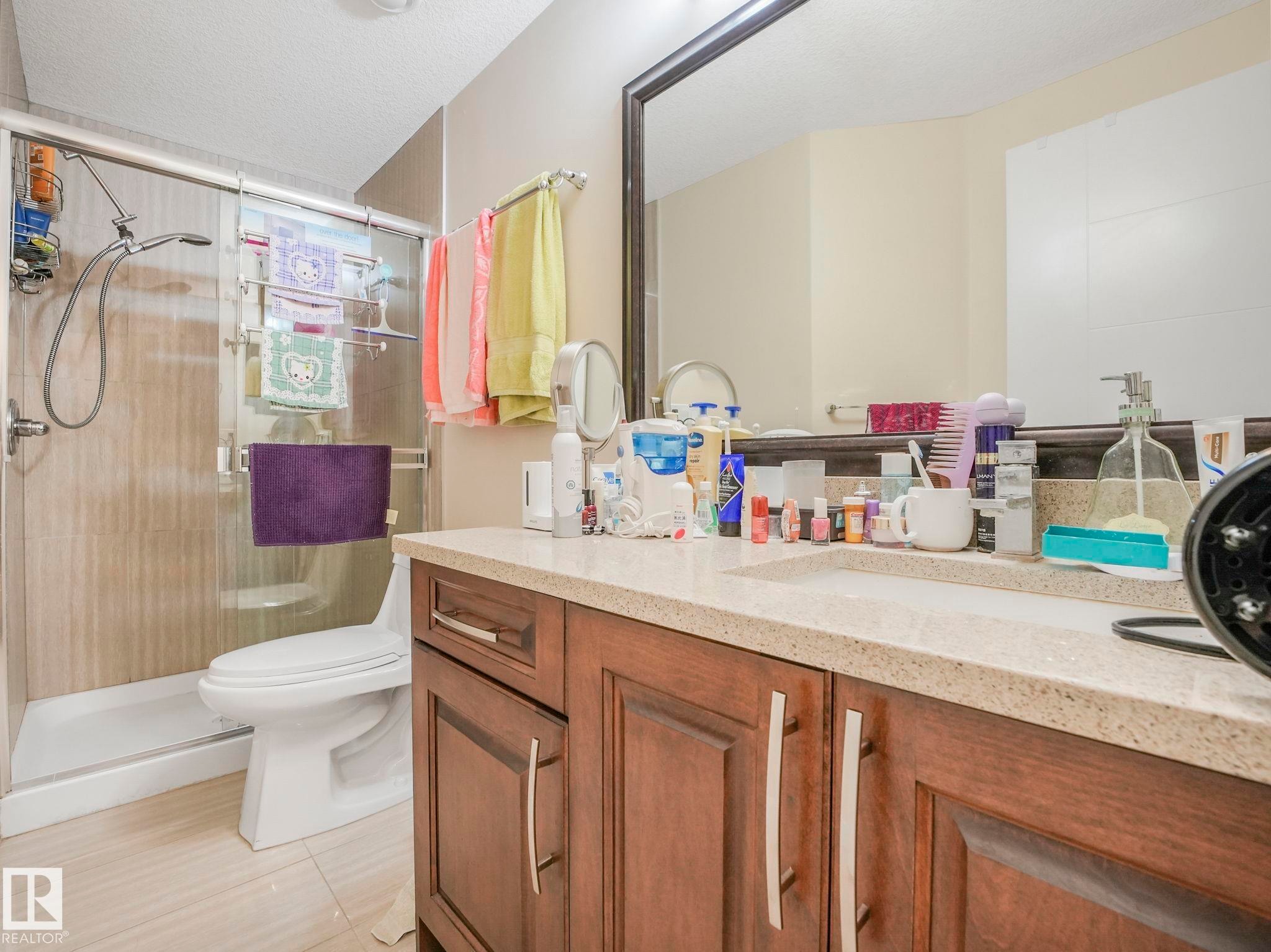 Bathroom featuring a single vanity with wood cabinetry, a light-toned countertop, and a large wall-mounted mirror - 3910 49 Avenue, Beaumont, AB - Indoor Photo Showing Bathroom