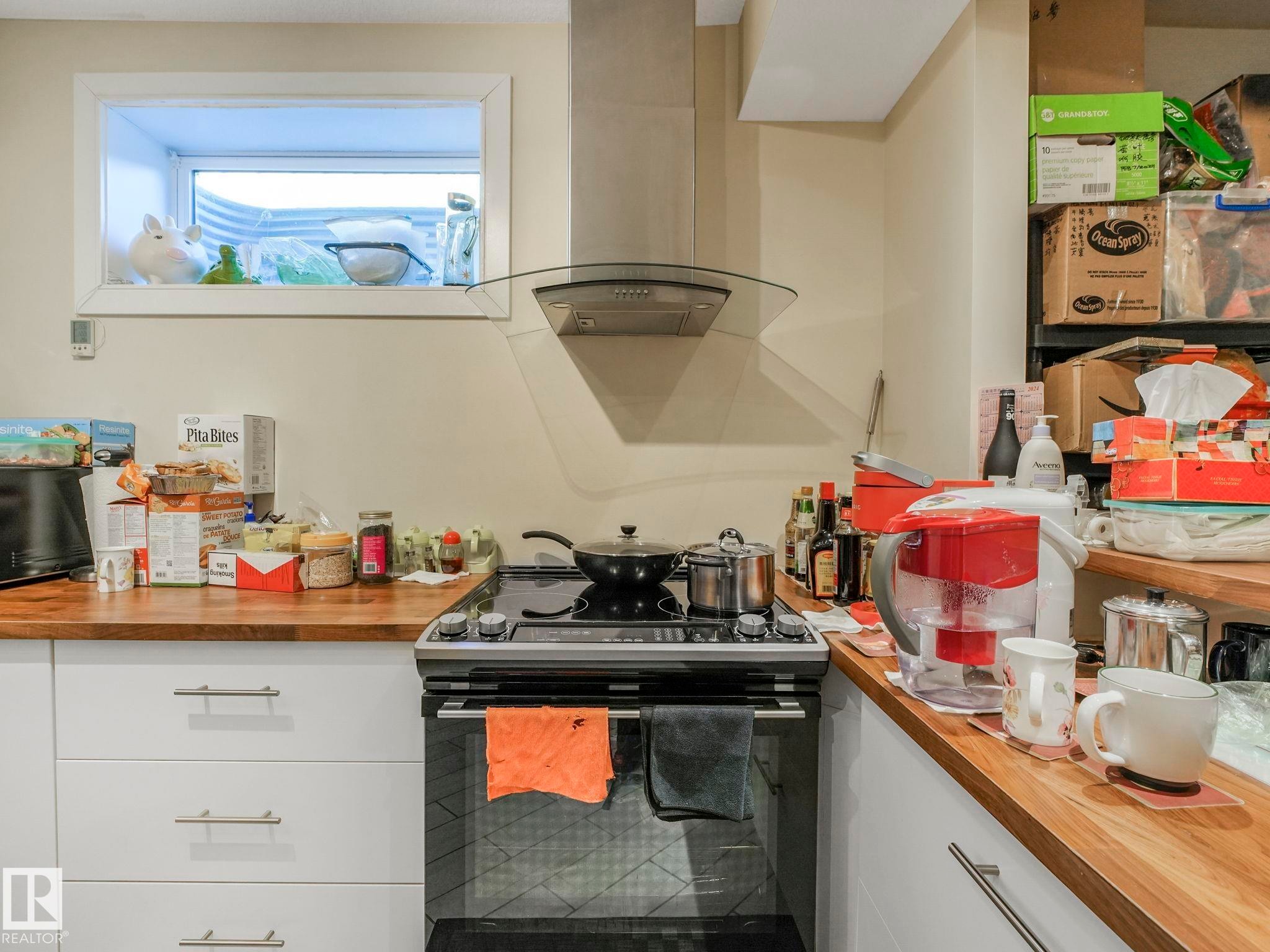 Kitchen featuring wood-finish countertops, white cabinetry with brushed nickel hardware, a stainless steel range, and a glass canopy range hood - 3910 49 Avenue, Beaumont, AB - Indoor Photo Showing Kitchen