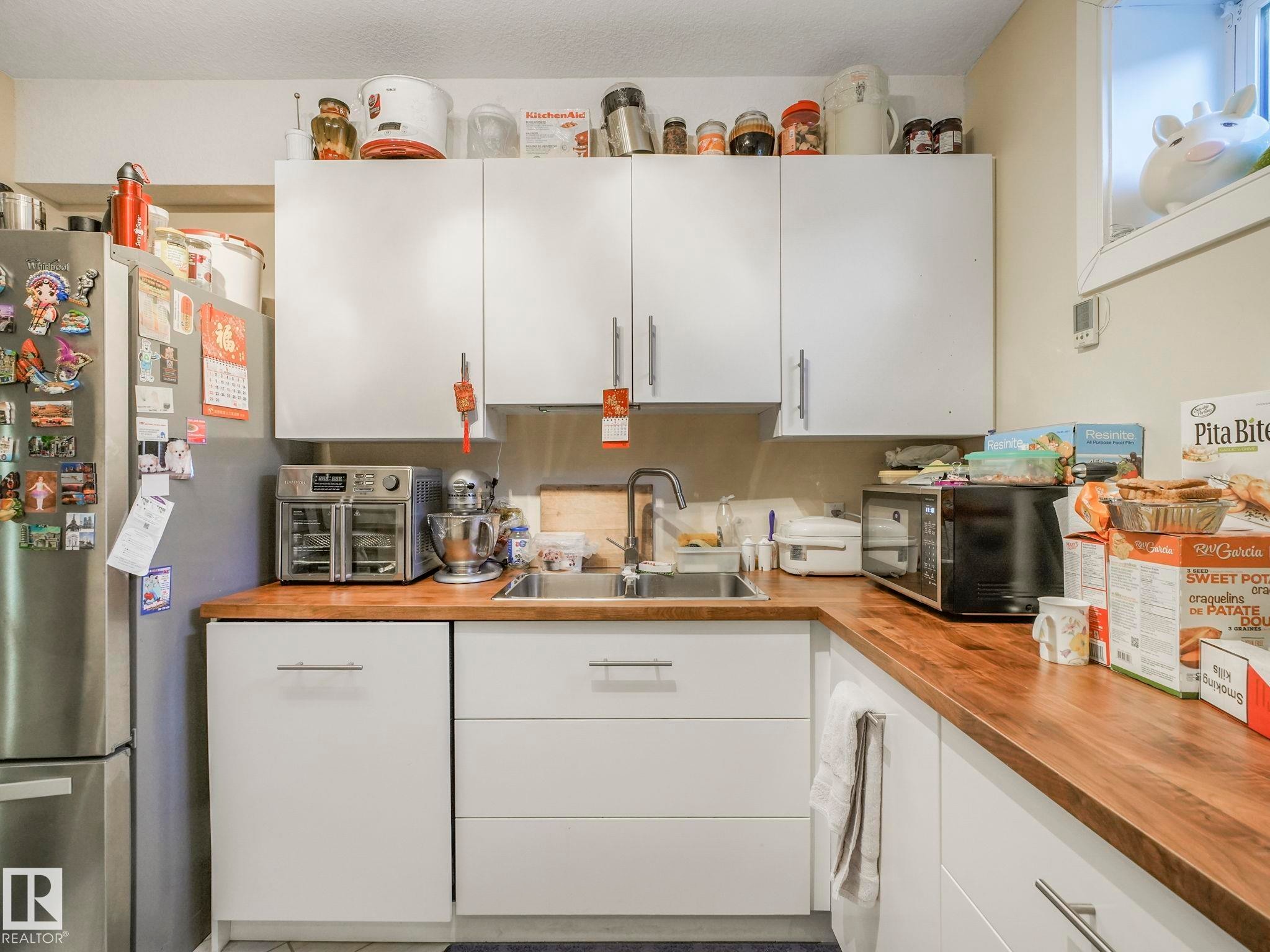 Kitchen featuring white cabinetry with silver-tone hardware, wood-finish countertops, a stainless steel sink with a single-handle faucet, and an integrated stainless steel refrigerator - 3910 49 Avenue, Beaumont, AB - Indoor Photo Showing Kitchen