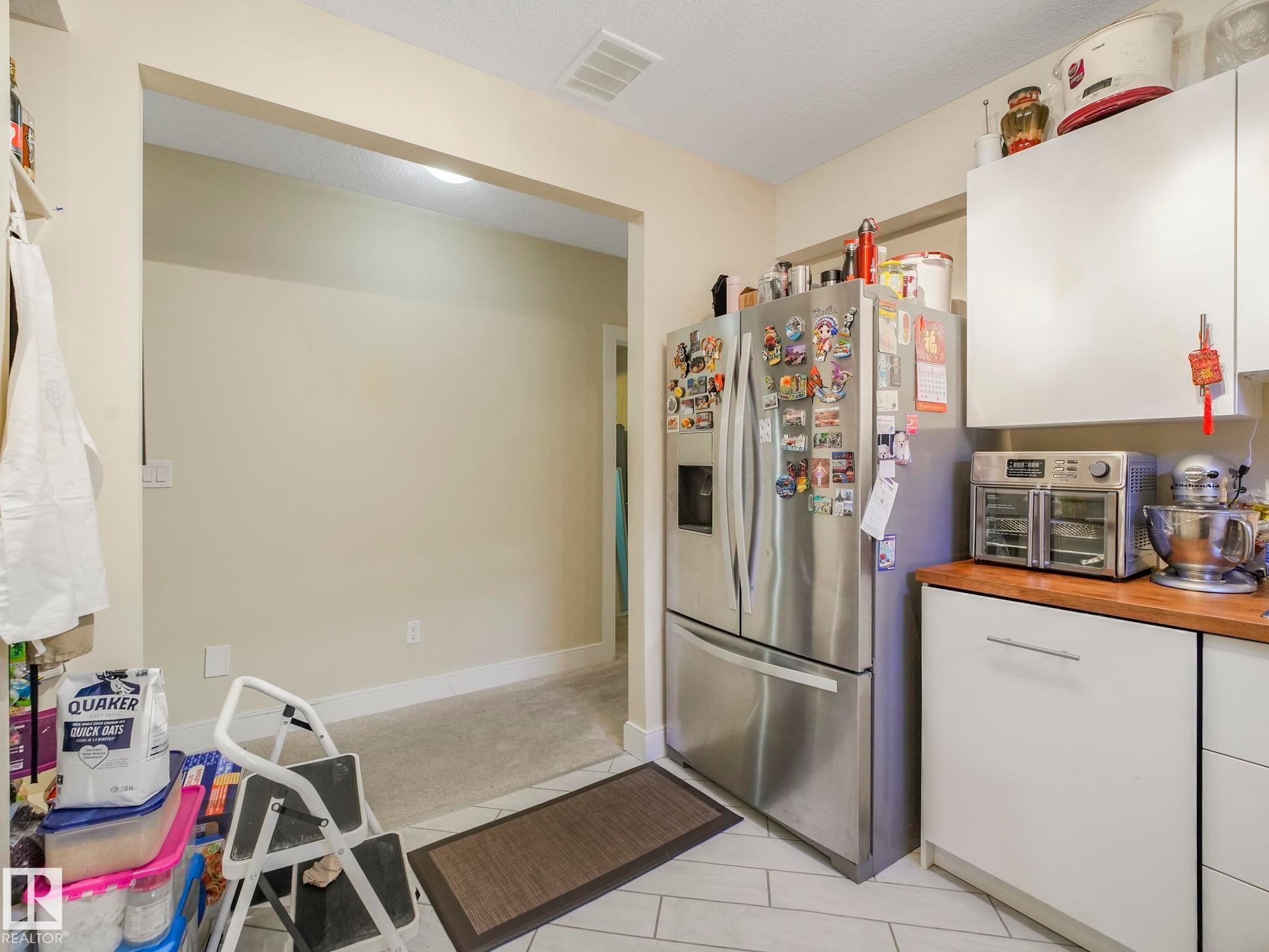 Kitchen area featuring white cabinetry, a wood-finish countertop, and tile flooring - 3910 49 Avenue, Beaumont, AB - Indoor
