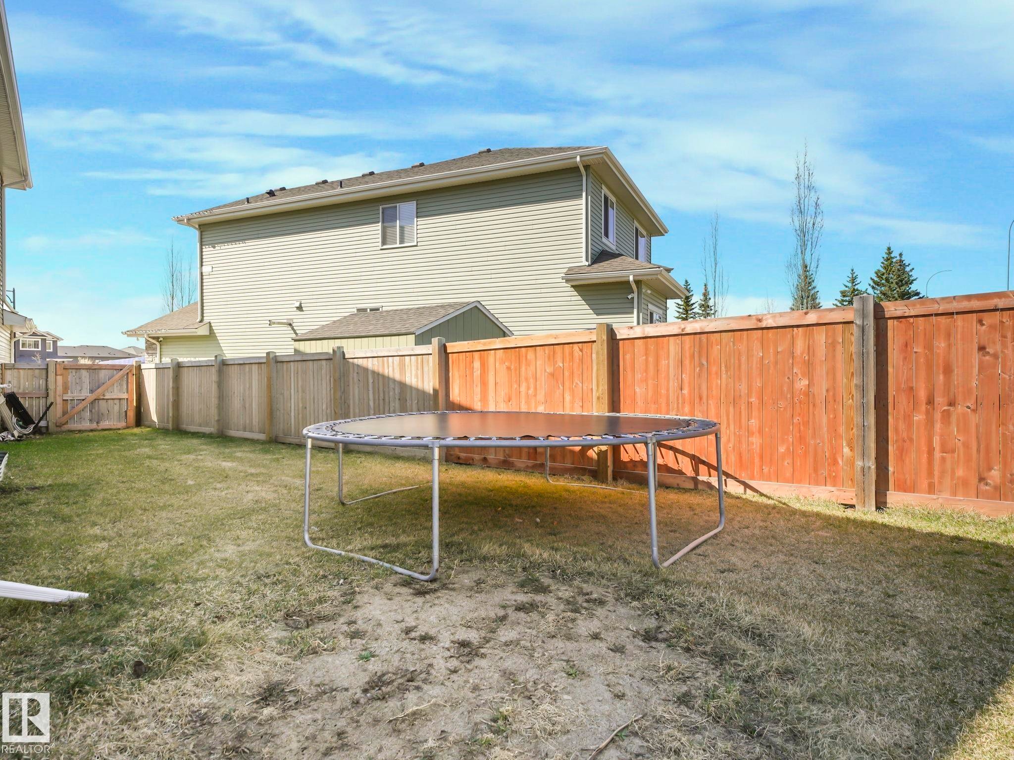 Expansive yard featuring a combination of wood privacy fencing and natural wood fencing, a mature lawn, and a two-story exterior with light siding - 3910 49 Avenue, Beaumont, AB - Outdoor
