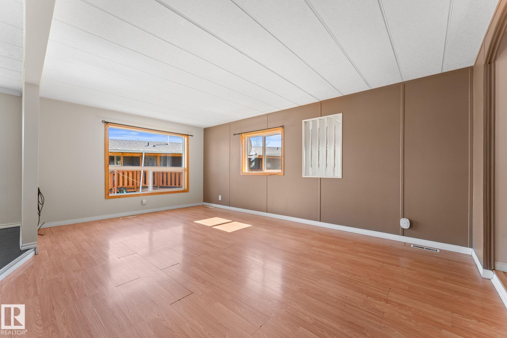 Spacious room featuring wood-finish flooring and multiple windows with wood trim - 4508 50A Avenue, Barrhead, AB - Indoor