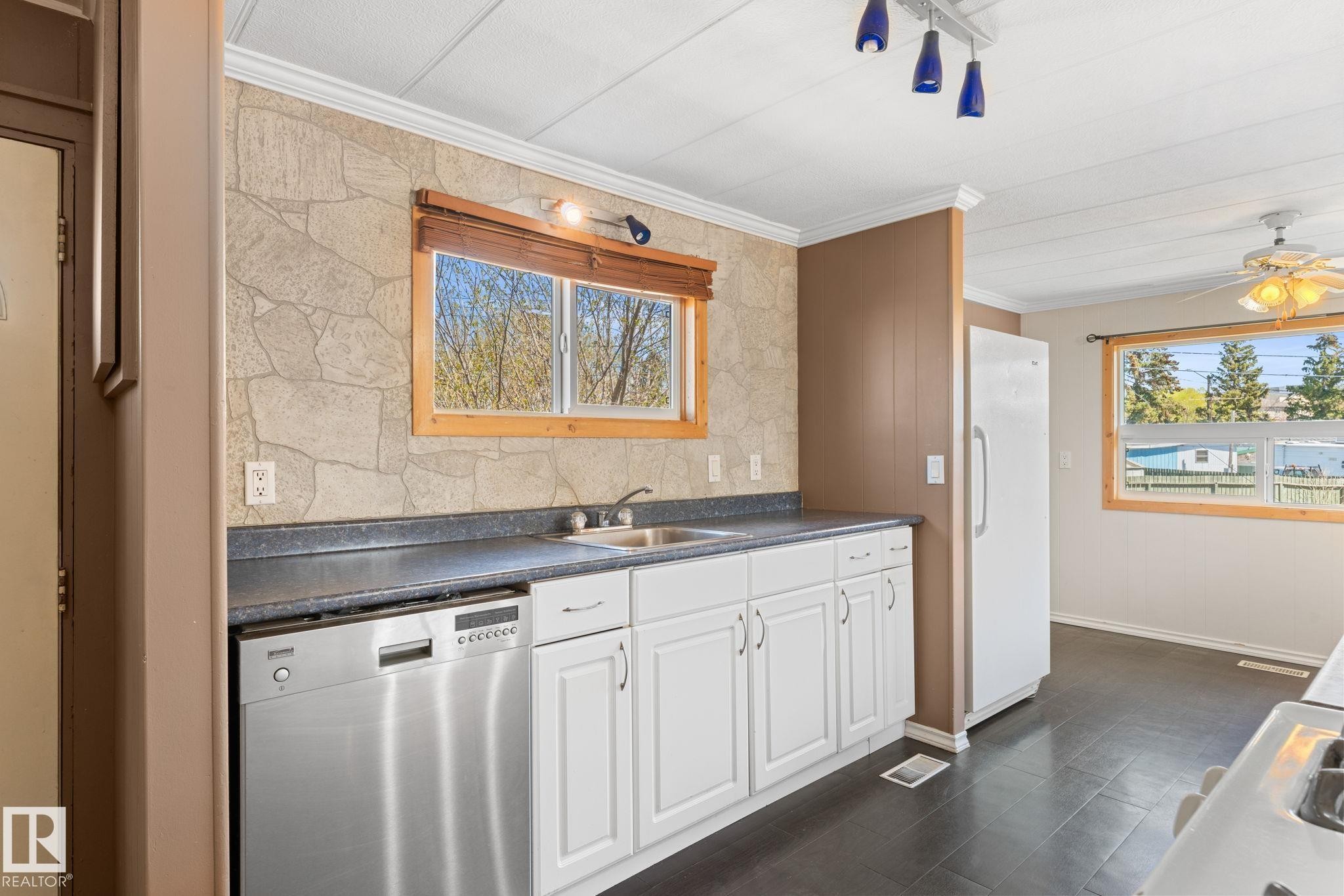 Kitchen featuring white cabinetry, dark speckled countertops, and a stone-look backsplash - 4508 50A Avenue, Barrhead, AB - Indoor Photo Showing Kitchen