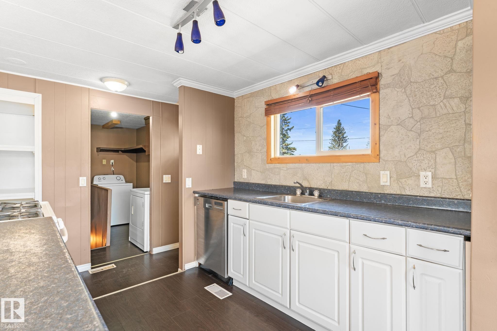 Kitchen area featuring white cabinetry, dark countertops, and a stainless steel dishwasher - 4508 50A Avenue, Barrhead, AB - Indoor