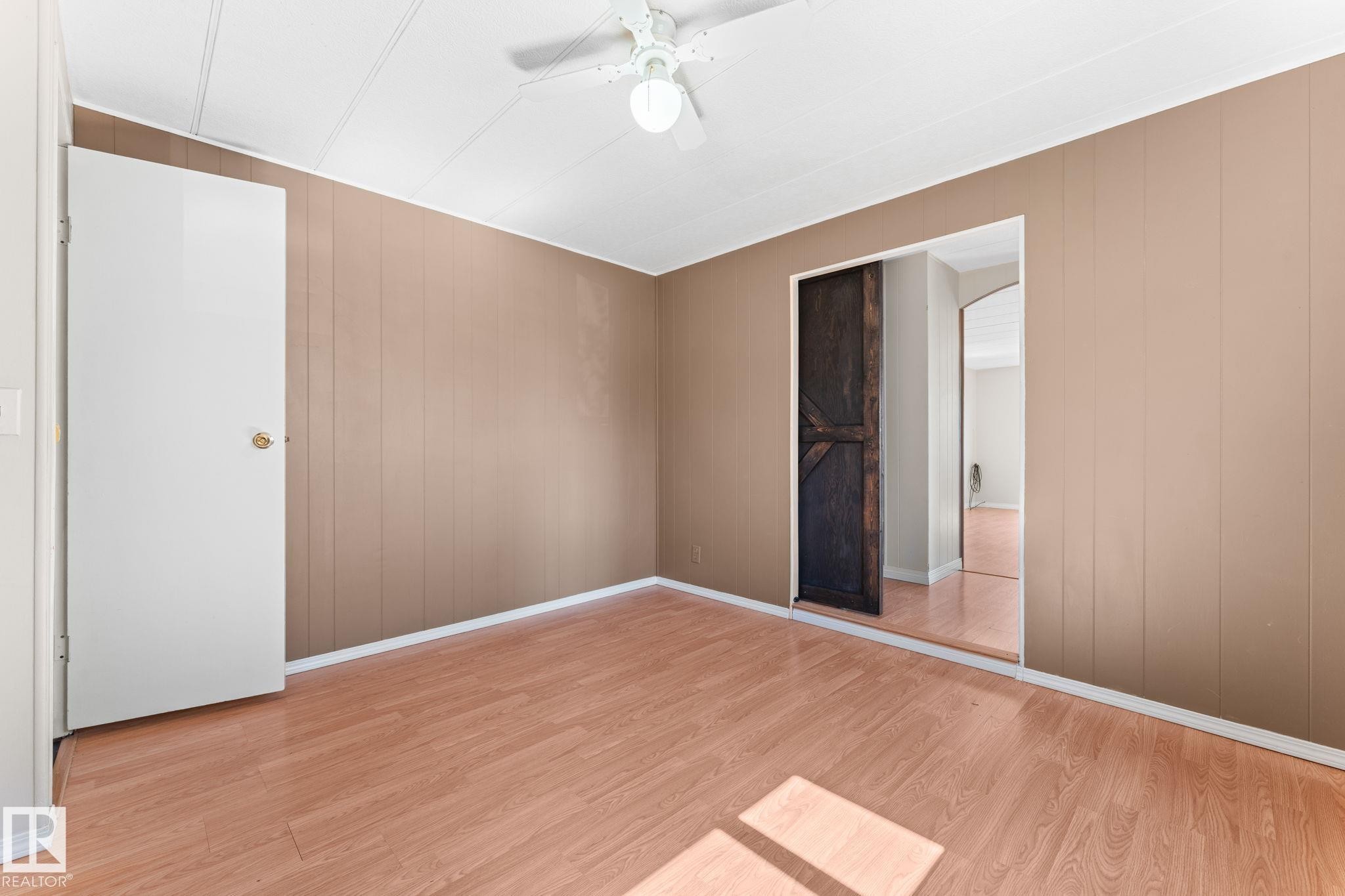 Room featuring wood-finish flooring, vertical paneling on walls, and a ceiling fan with integrated lighting - 4508 50A Avenue, Barrhead, AB - Indoor Photo Showing Other Room