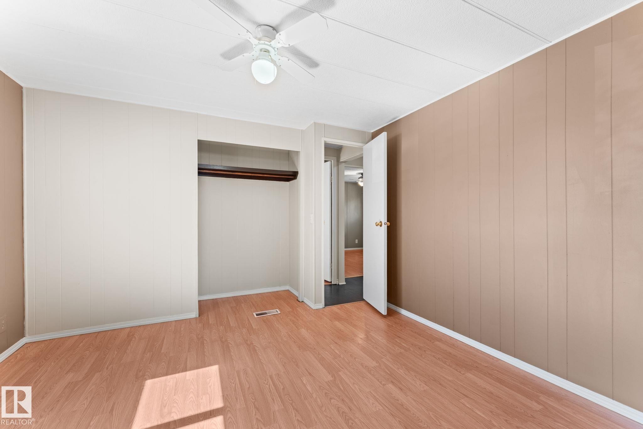 Room featuring wood-finish flooring, a built-in closet with a hanging rod, a ceiling fan with integrated lighting, and neutral wall tones - 4508 50A Avenue, Barrhead, AB - Indoor Photo Showing Other Room