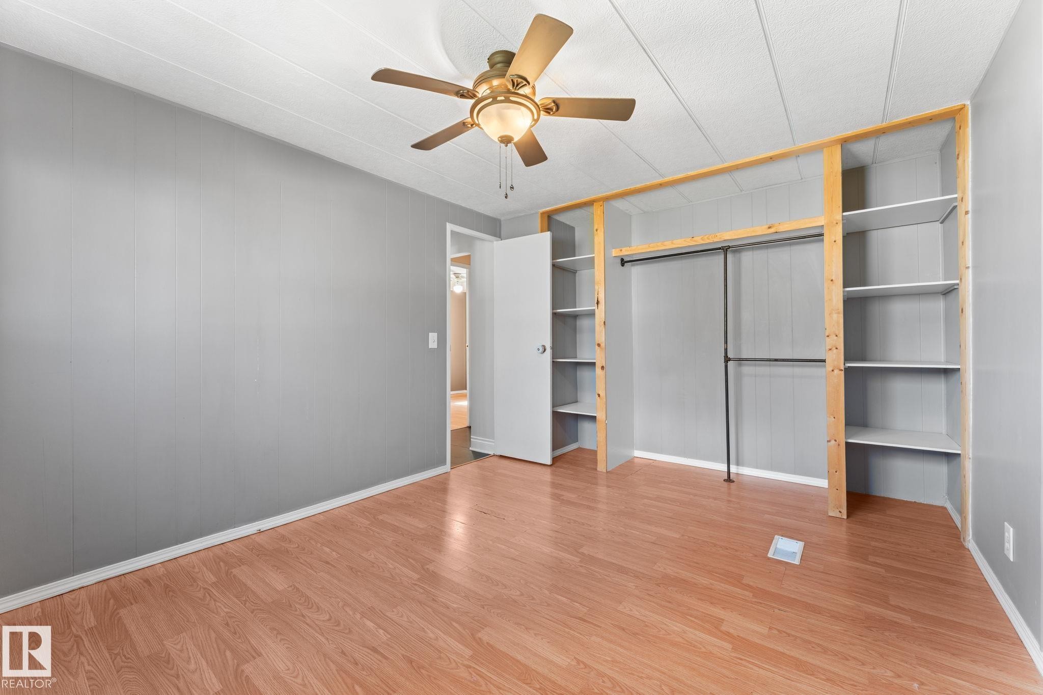 Room featuring wood-finish flooring, a ceiling fan with integrated lighting, and a built-in shelving unit with a clothing rod - 4508 50A Avenue, Barrhead, AB - Indoor Photo Showing Other Room