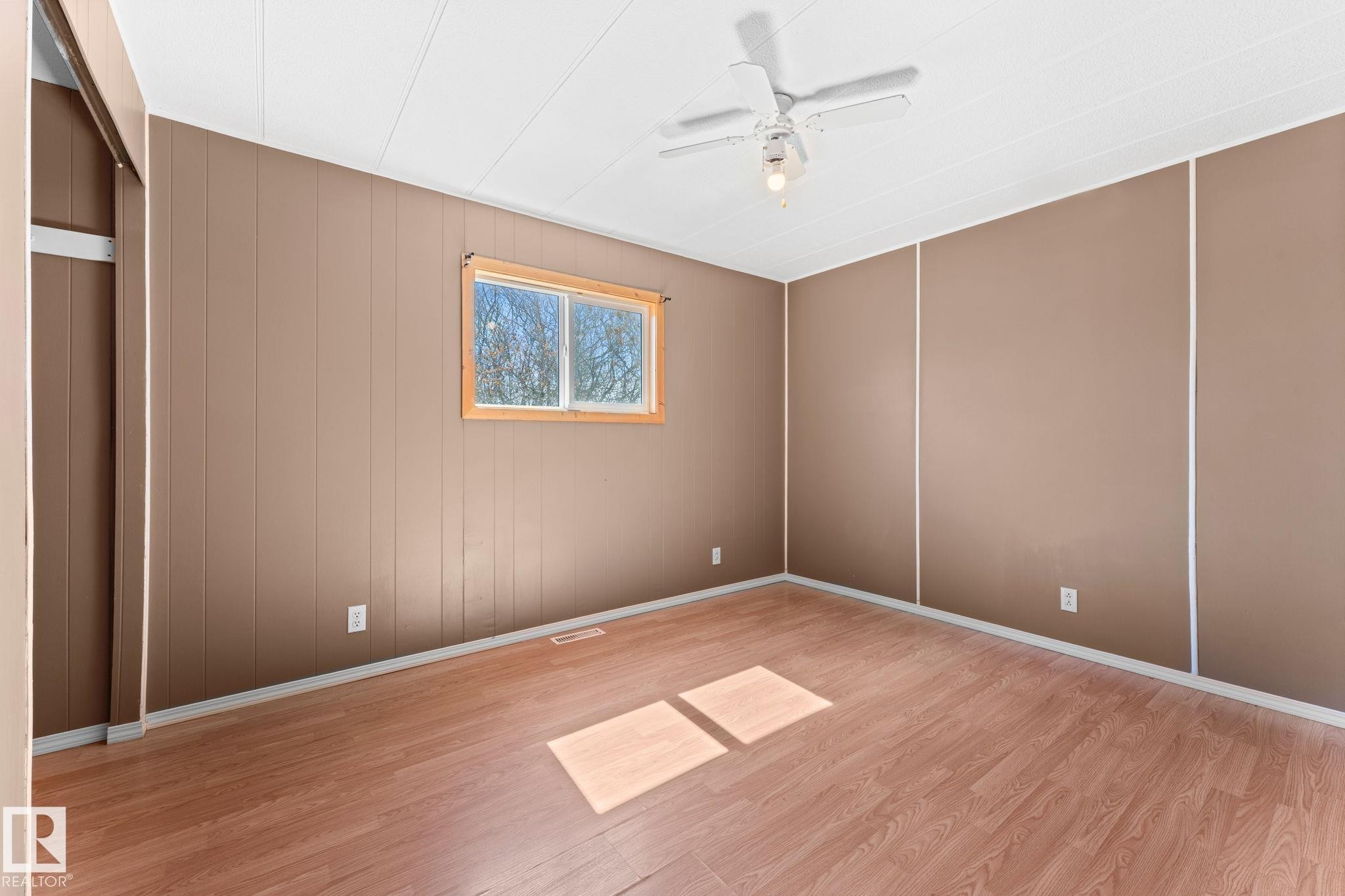Room featuring wood-finish flooring, a ceiling fan with light, and a window with wood trim - 4508 50A Avenue, Barrhead, AB - Indoor Photo Showing Other Room