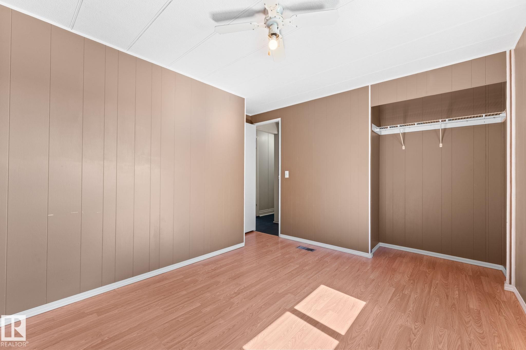 Room featuring wood-finish flooring, vertical panel wall accents, a ceiling fan with integrated lighting, and an open closet with shelving and hanging rods - 4508 50A Avenue, Barrhead, AB - Indoor Photo Showing Other Room