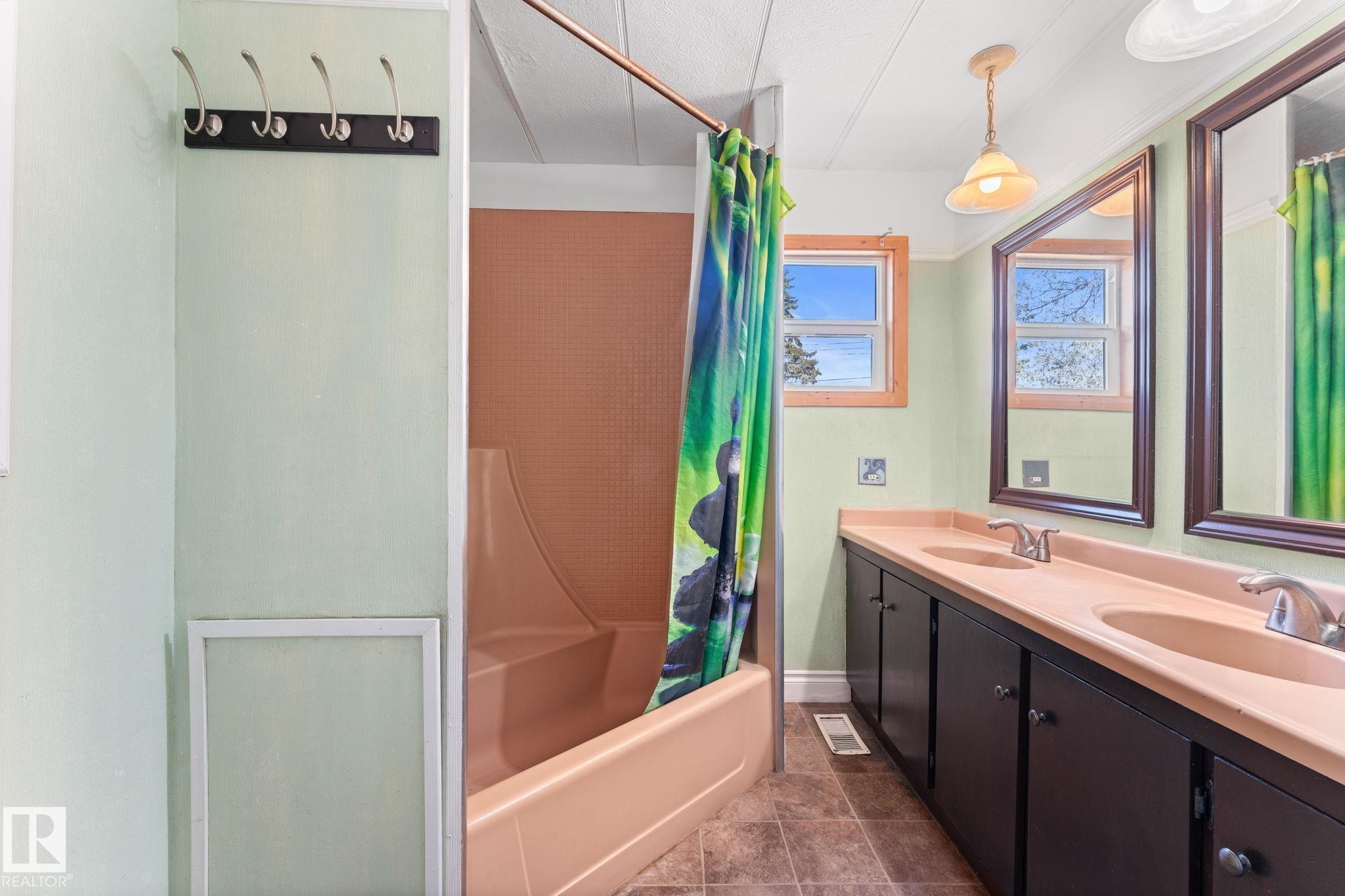 Bathroom featuring a double vanity with built-in cabinetry, dual mirrors, a window with wood trim, and a shower-tub combination - 4508 50A Avenue, Barrhead, AB - Indoor Photo Showing Bathroom