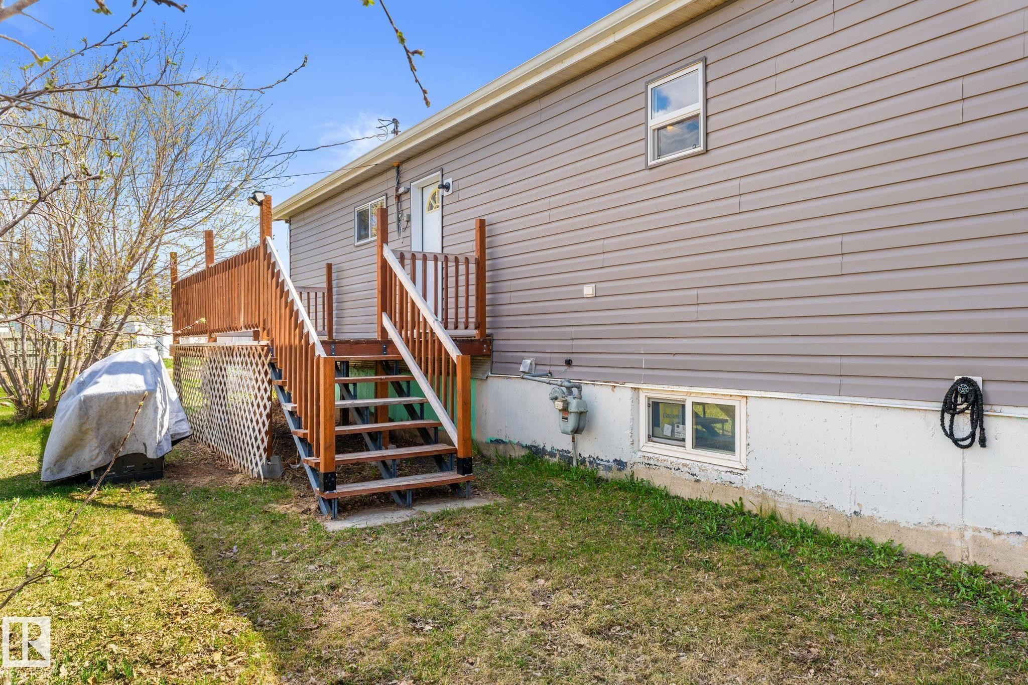 Rear exterior featuring a wooden deck with railing, stairs, and lattice skirting - 4508 50A Avenue, Barrhead, AB - Outdoor With Exterior
