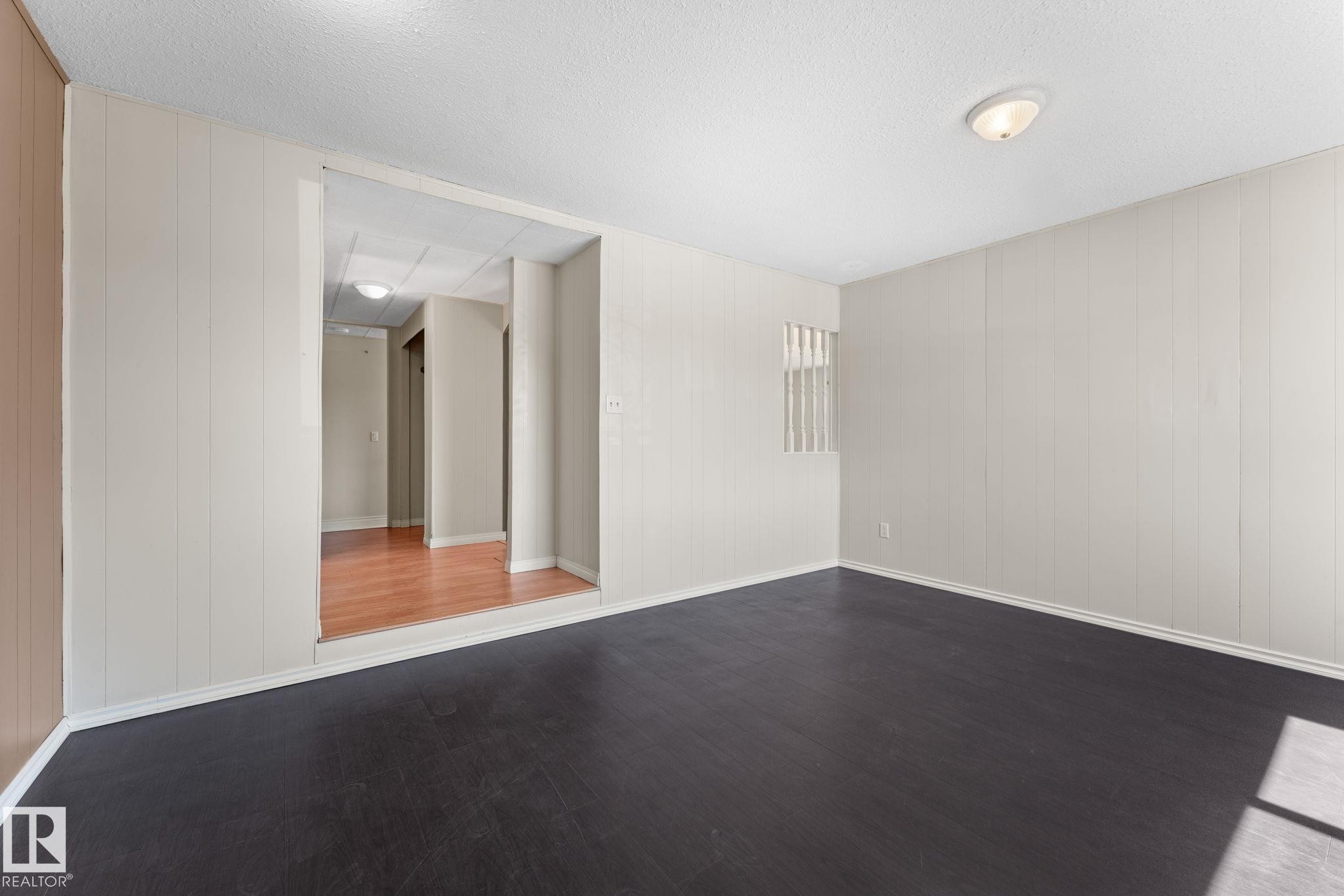 Spacious room featuring dark wood-finish flooring, light-toned vertical paneling, and white baseboards - 4508 50A Avenue, Barrhead, AB - Indoor Photo Showing Other Room