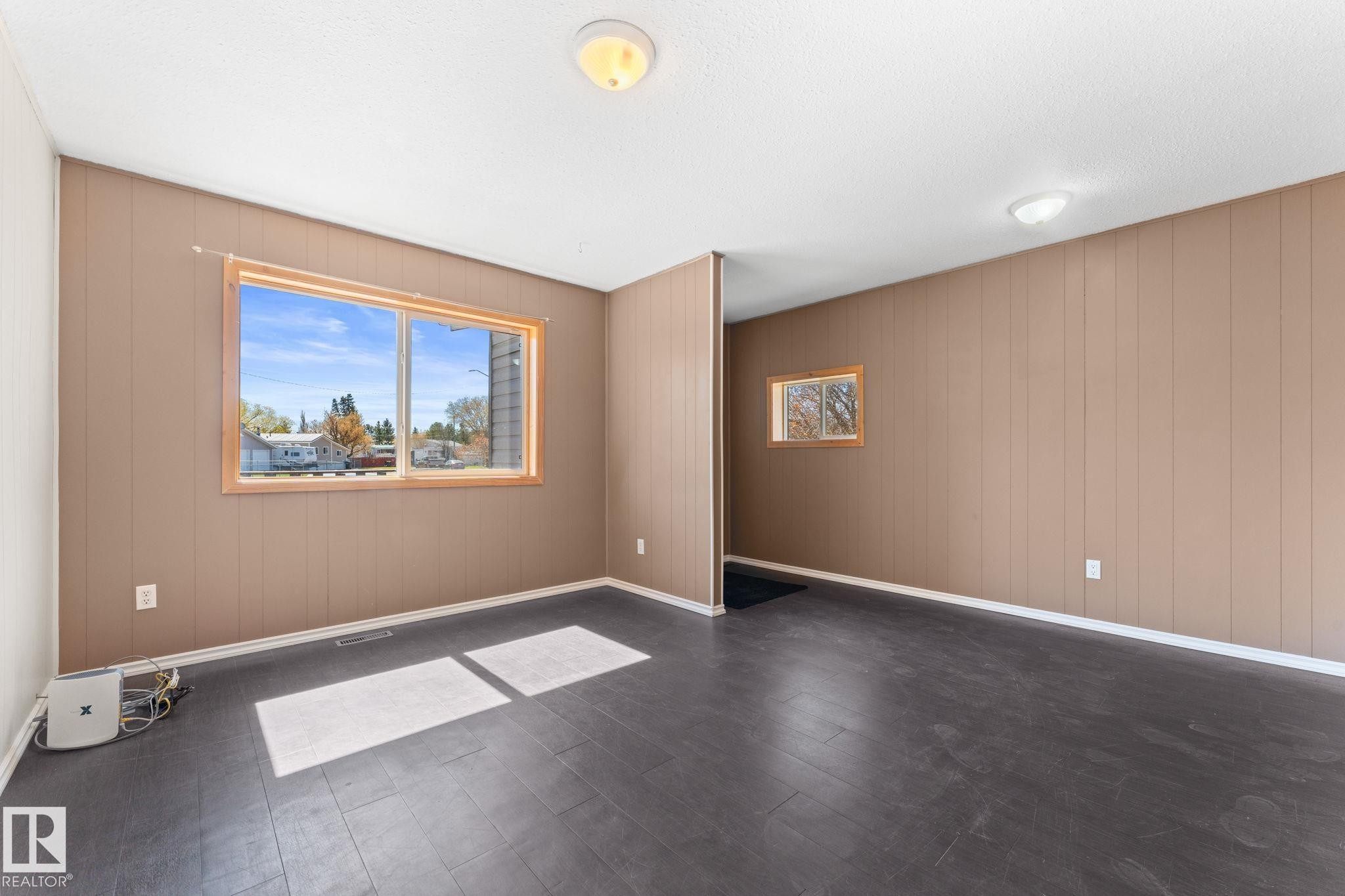 Spacious room featuring wood-finish flooring, two windows with wood trim, and vertical paneling - 4508 50A Avenue, Barrhead, AB - Indoor Photo Showing Other Room