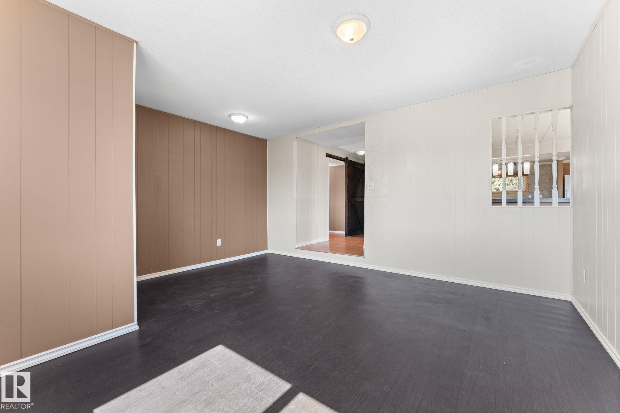 Spacious room featuring dark wood-finish flooring, two-tone paneling, and an interior pass-through window with white vertical slats - 4508 50A Avenue, Barrhead, AB - Indoor Photo Showing Other Room
