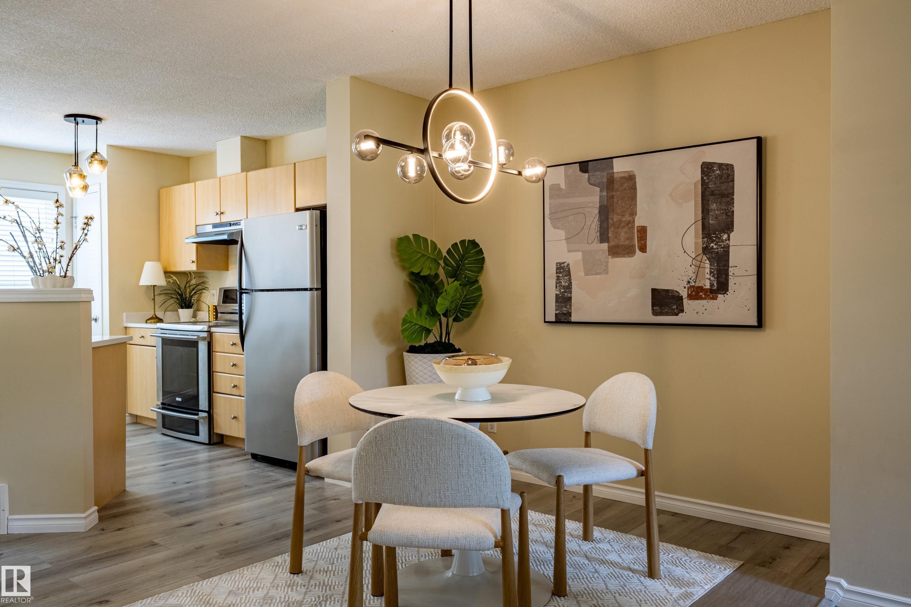 Dining area featuring a contemporary chandelier, a round white table, and four upholstered chairs - 41 8304 11 Avenue, Edmonton, AB - Indoor Photo Showing Dining Room