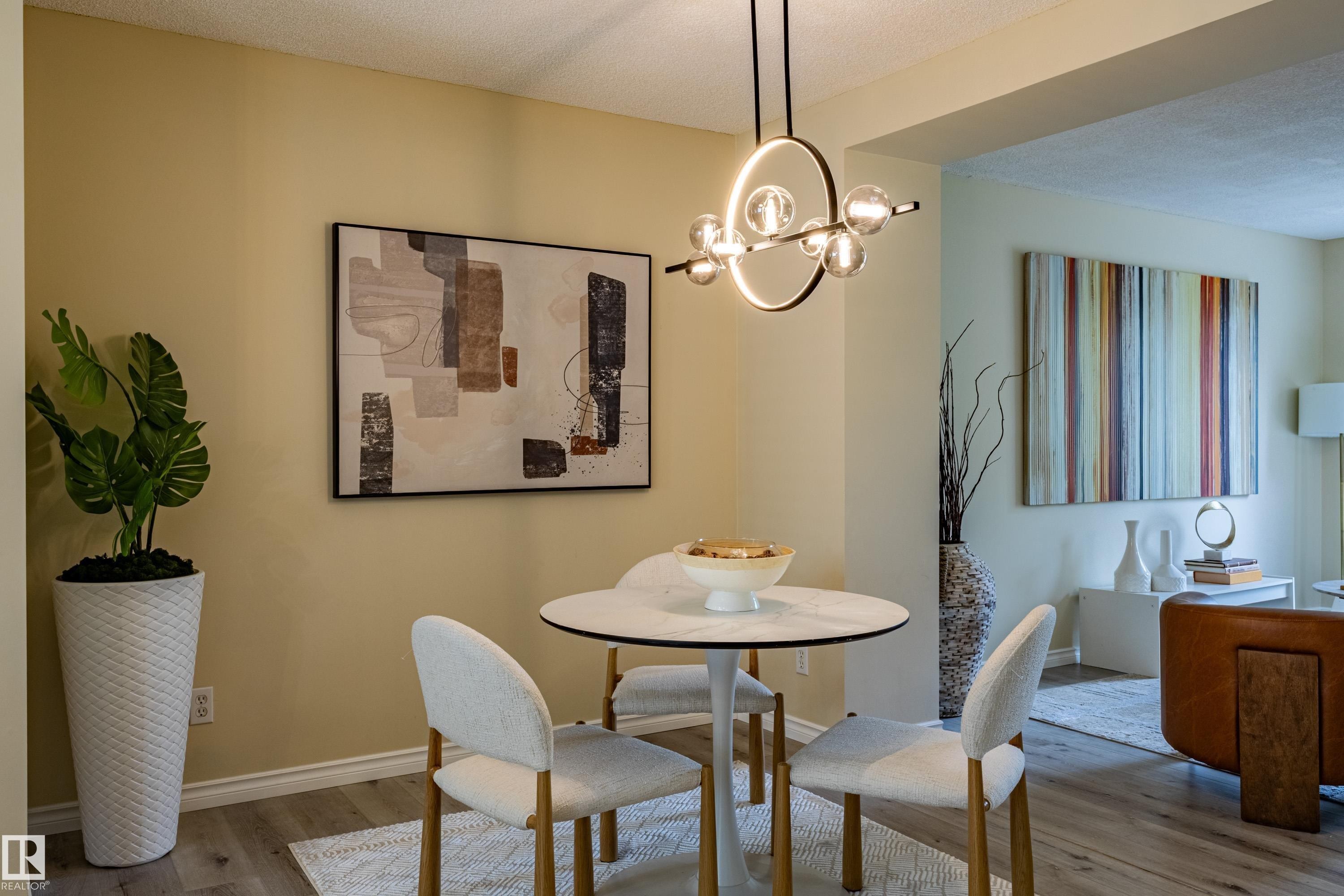 Dining area featuring a contemporary chandelier, light-toned walls, wood-finish flooring, and an archway opening to an additional room - 41 8304 11 Avenue, Edmonton, AB - Indoor Photo Showing Dining Room