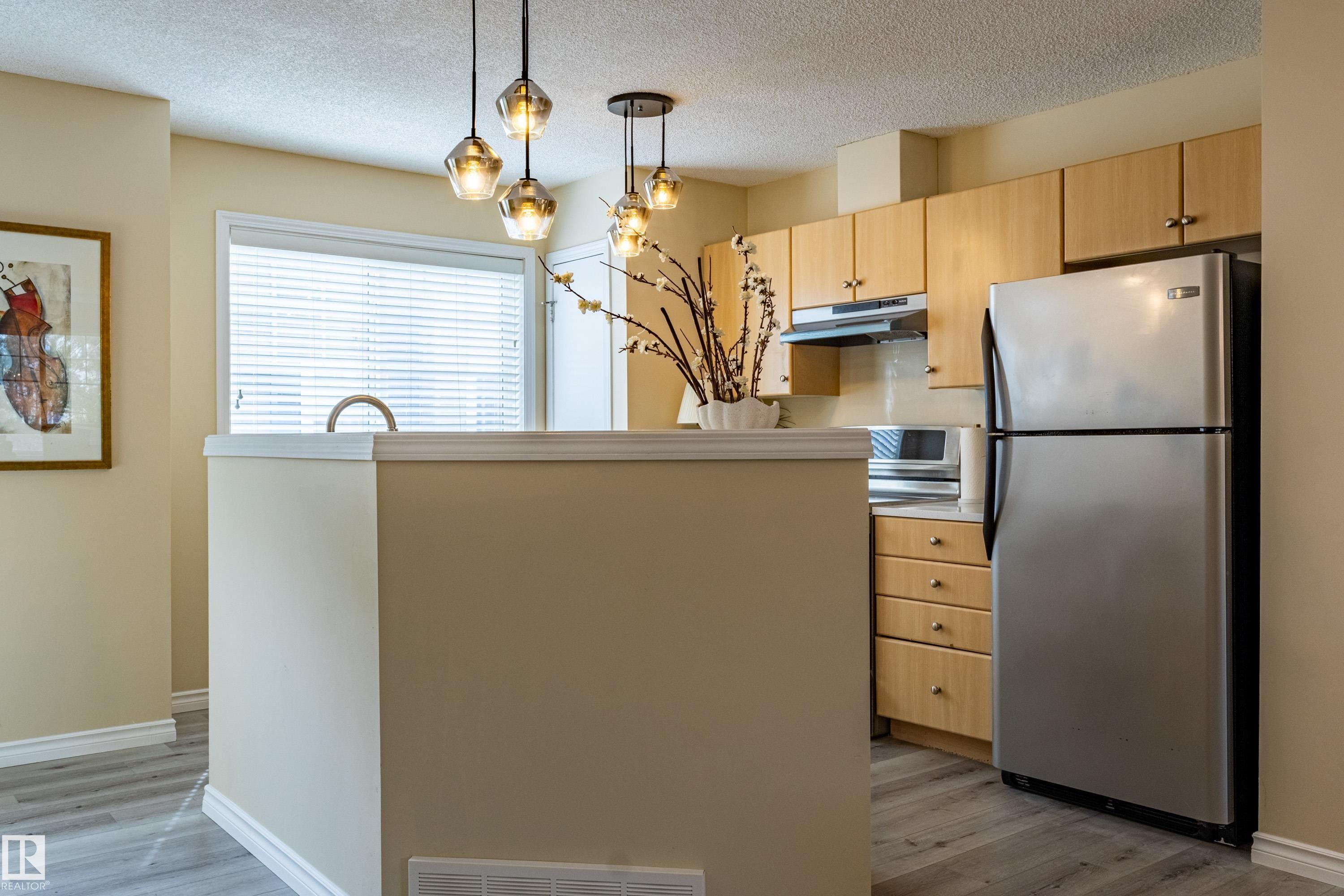 Kitchen featuring light wood-finish cabinetry, stainless steel refrigerator, and wood-finish flooring - 41 8304 11 Avenue, Edmonton, AB - Indoor Photo Showing Kitchen