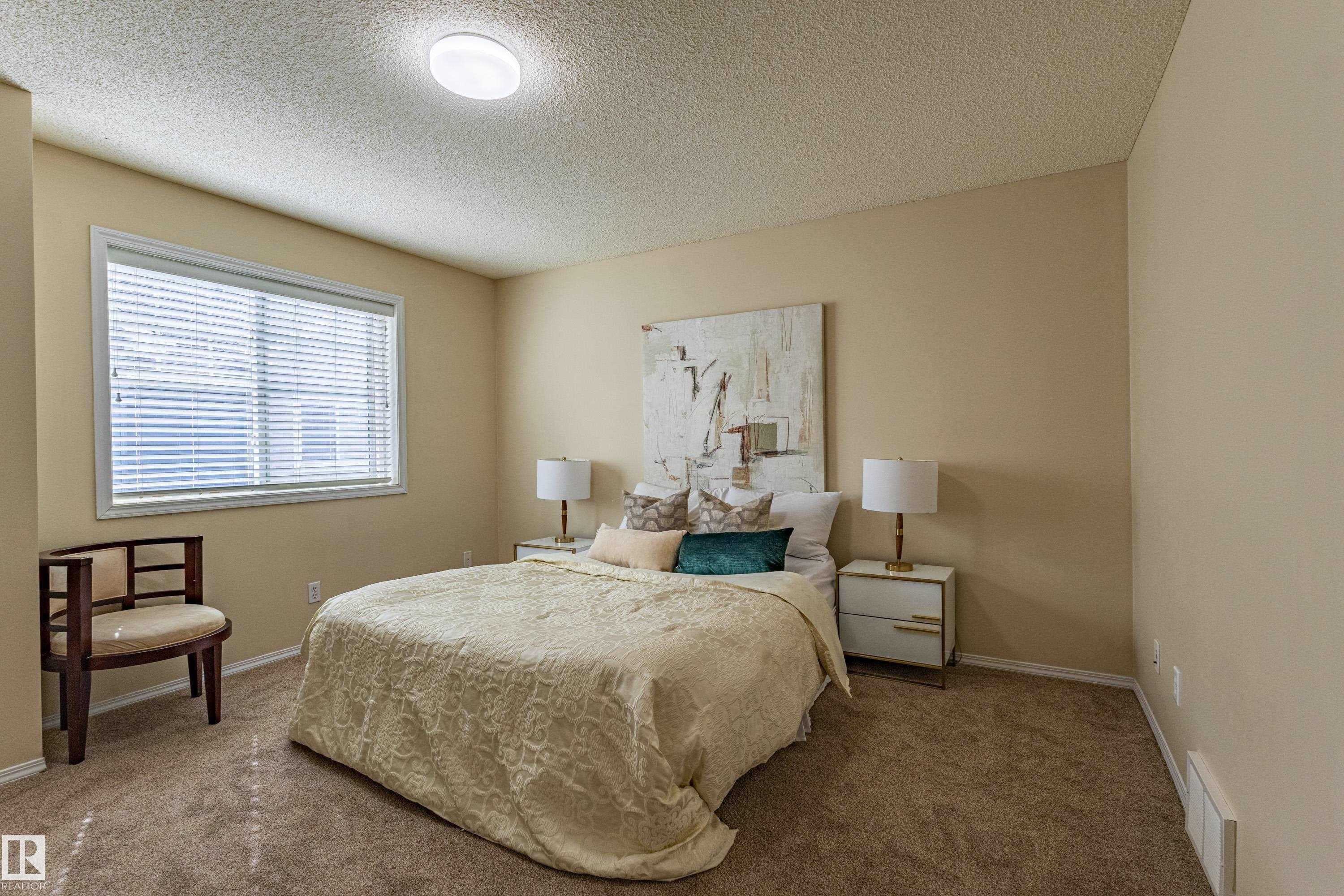 Carpeted room with a large window featuring horizontal blinds, a white window frame, and neutral-toned walls - 41 8304 11 Avenue, Edmonton, AB - Indoor Photo Showing Bedroom