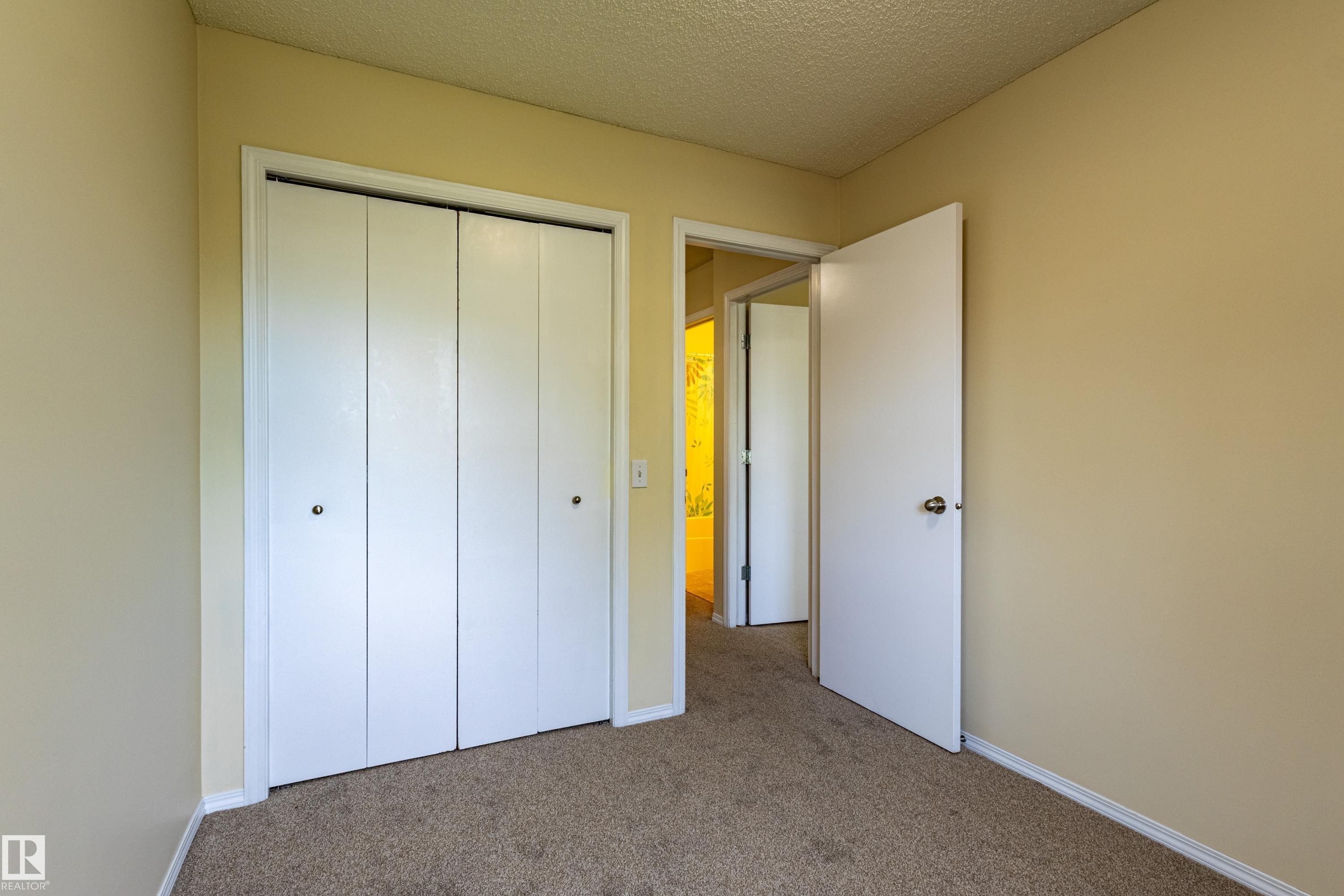 Neutral-toned carpeted room featuring a four-panel bi-fold closet with white doors and baseboards - 41 8304 11 Avenue, Edmonton, AB - Indoor