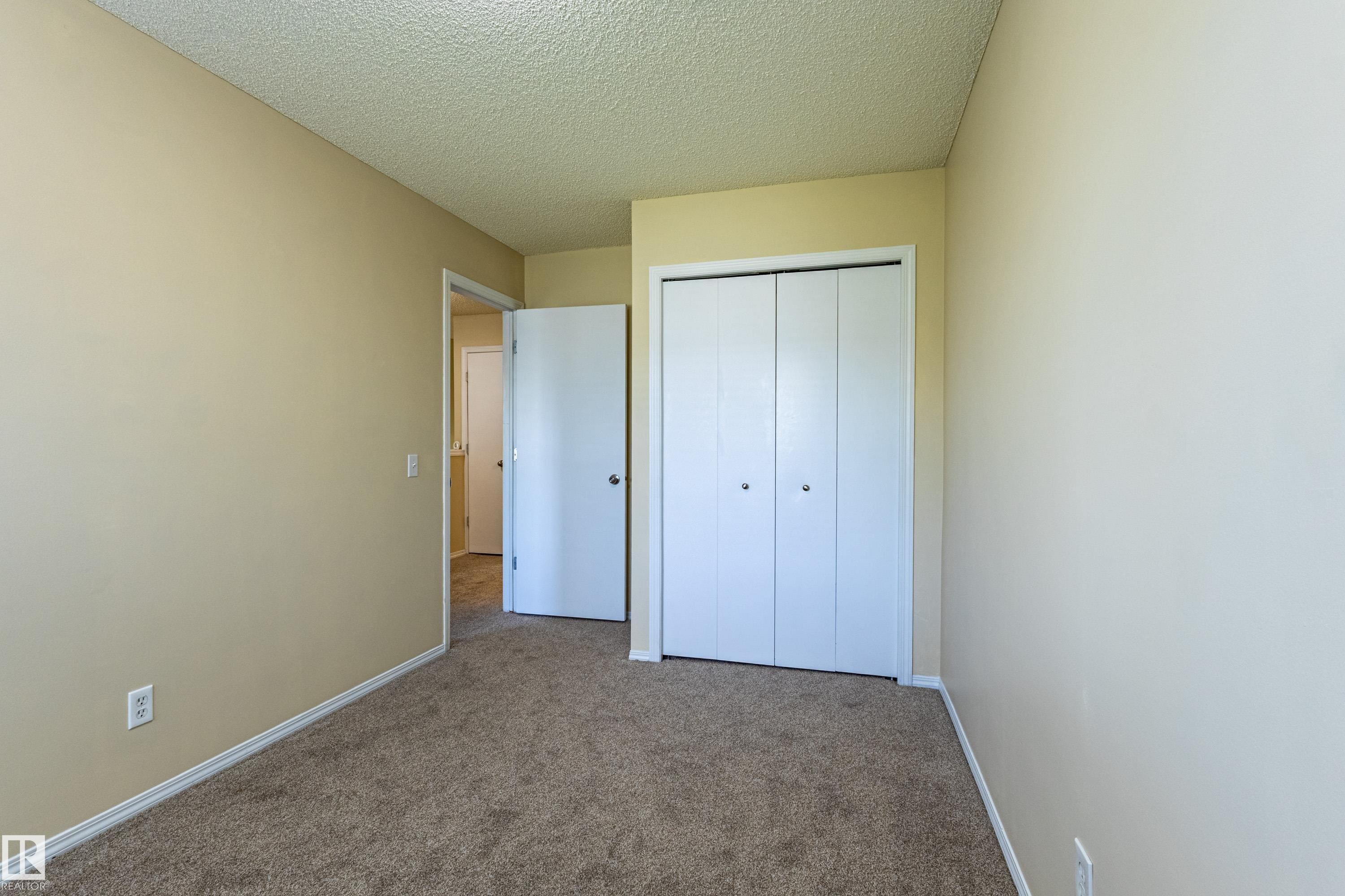 Carpeted room featuring neutral-toned walls, white baseboards, and a bi-fold closet door - 41 8304 11 Avenue, Edmonton, AB - Indoor Photo Showing Other Room