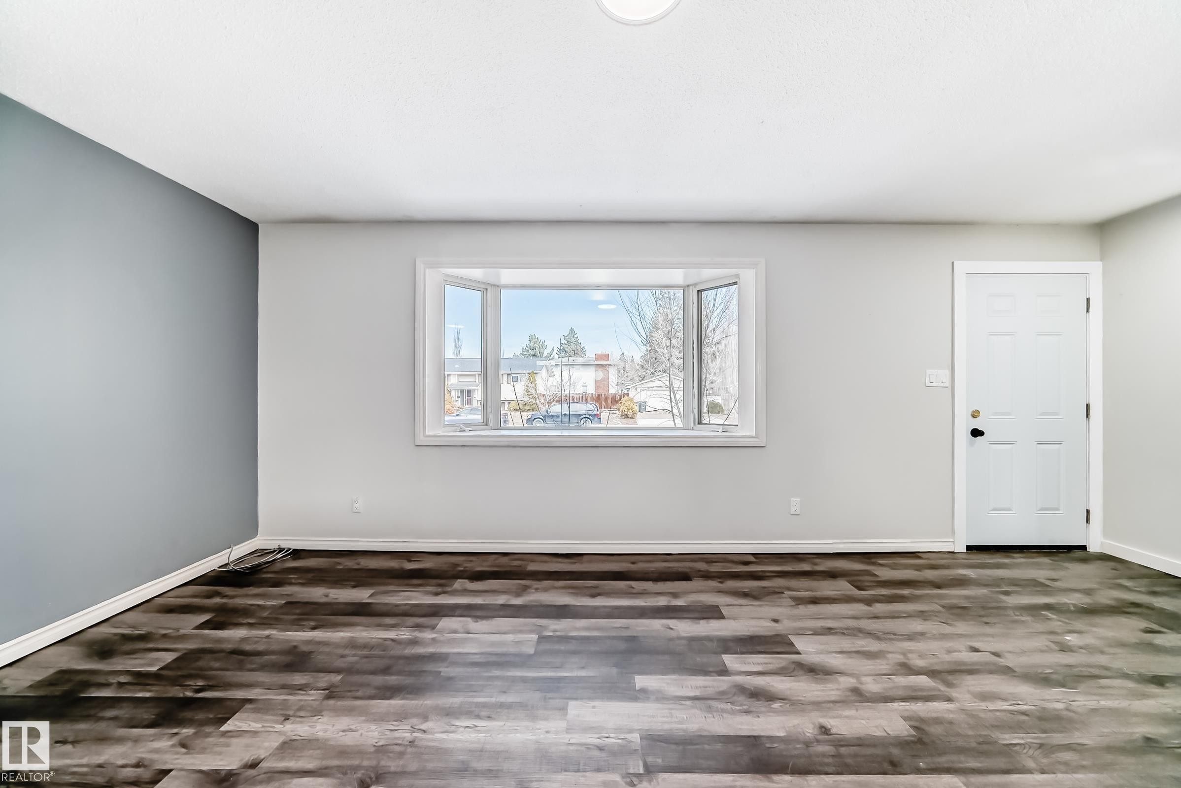 Bright interior space featuring a multi-pane bay window, dark wood-finish flooring, a contemporary accent wall, and a paneled entry door - 8615 42A Avenue, Edmonton, AB - Indoor Photo Showing Other Room