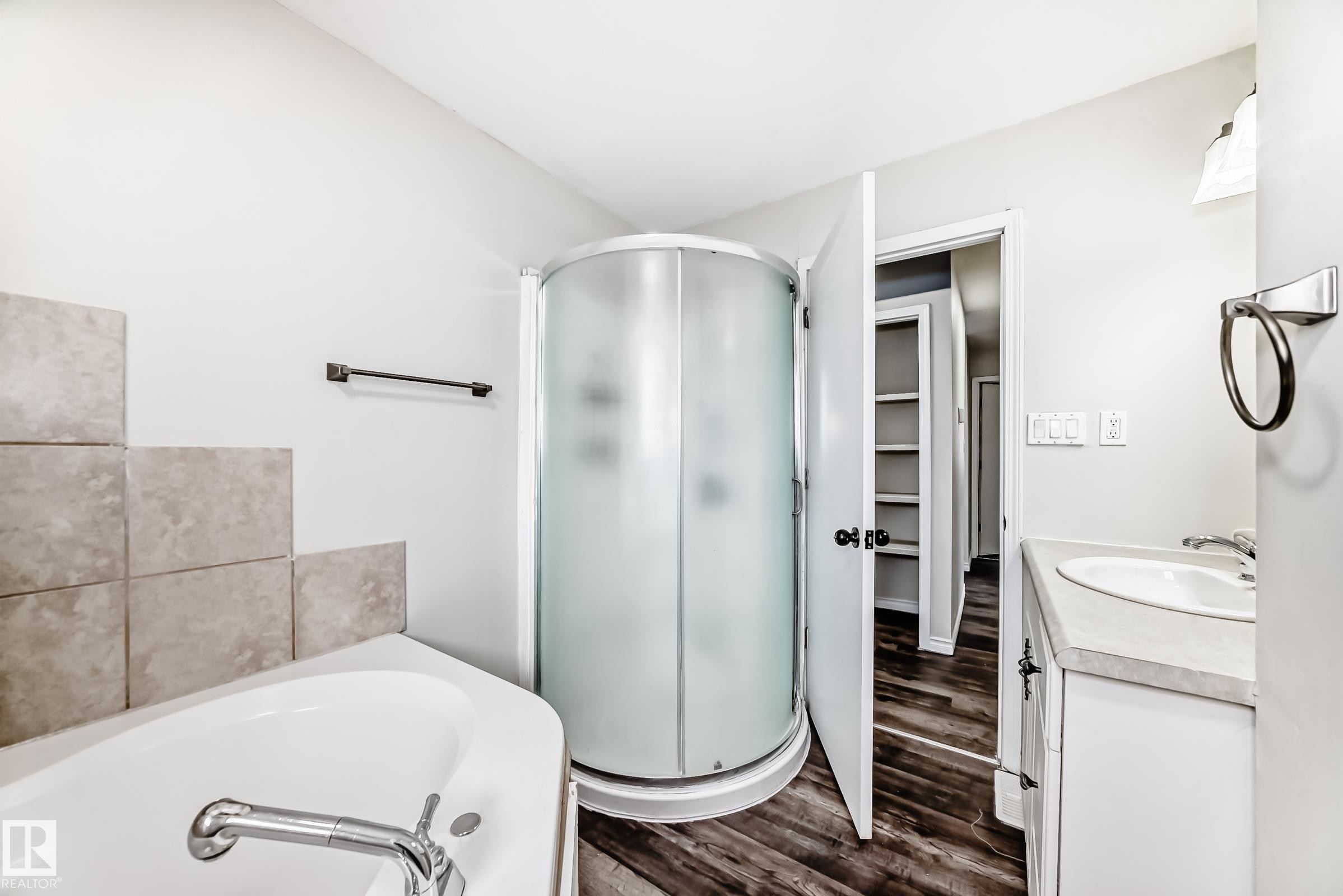 Bathroom featuring a corner shower, separate soaking tub with tile surround, single vanity with integrated sink, and wood-finish flooring - 8615 42A Avenue, Edmonton, AB - Indoor Photo Showing Bathroom