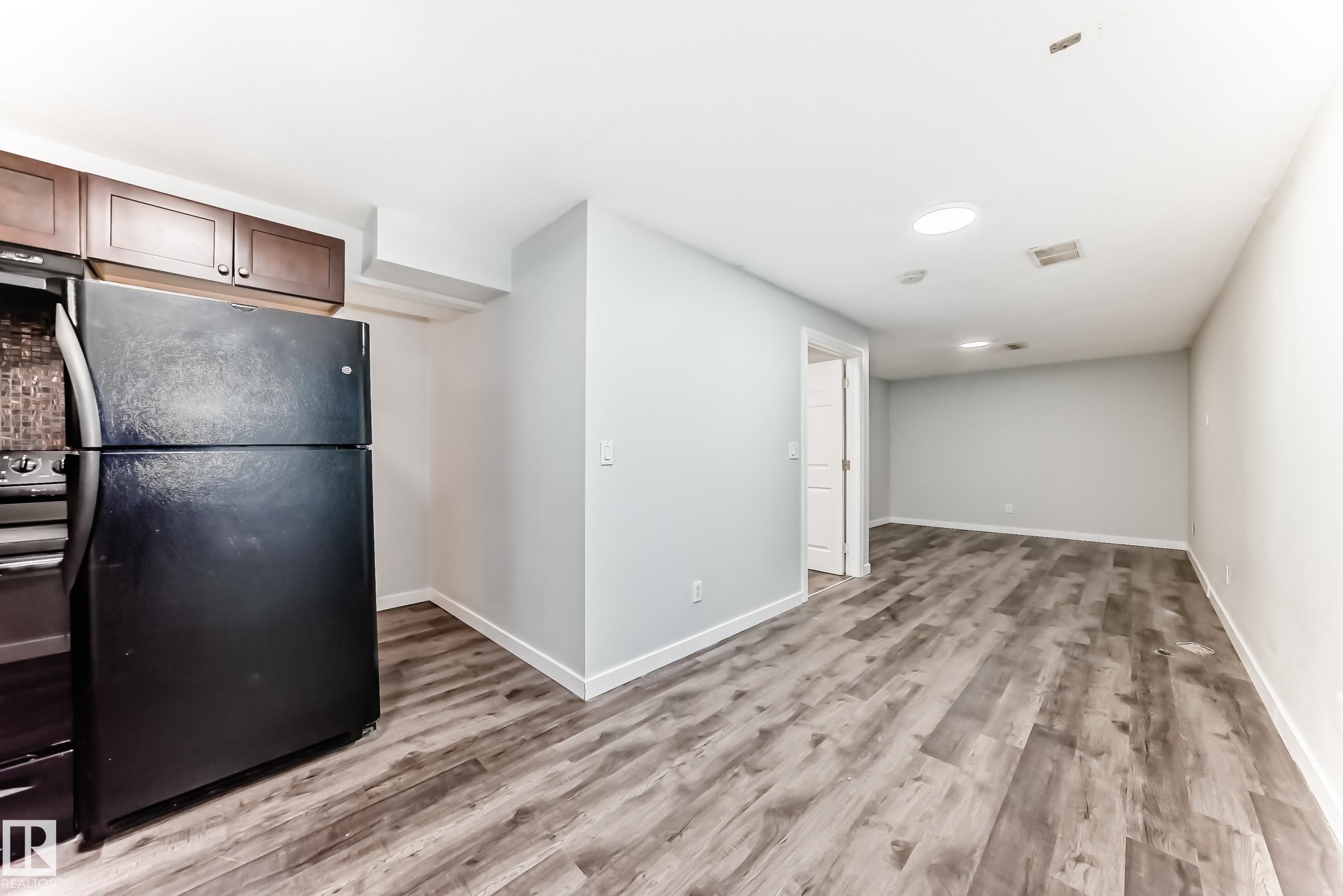 Kitchen area featuring a black refrigerator, dark wood cabinetry, and a mosaic tile backsplash - 8615 42A Avenue, Edmonton, AB - Indoor