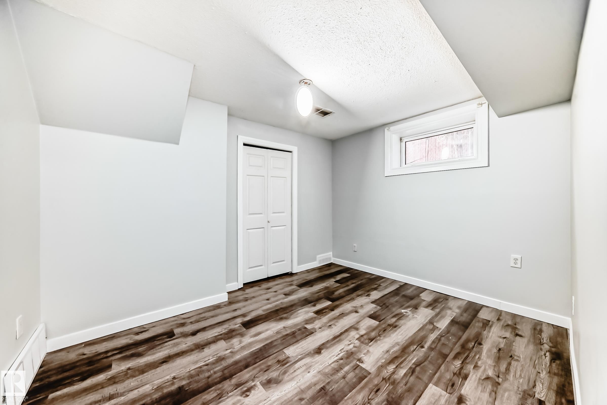 Room featuring wood-finish flooring, light gray walls, a white bi-fold closet, a single window, and a ceiling-mounted light fixture - 8615 42A Avenue, Edmonton, AB - Indoor Photo Showing Other Room
