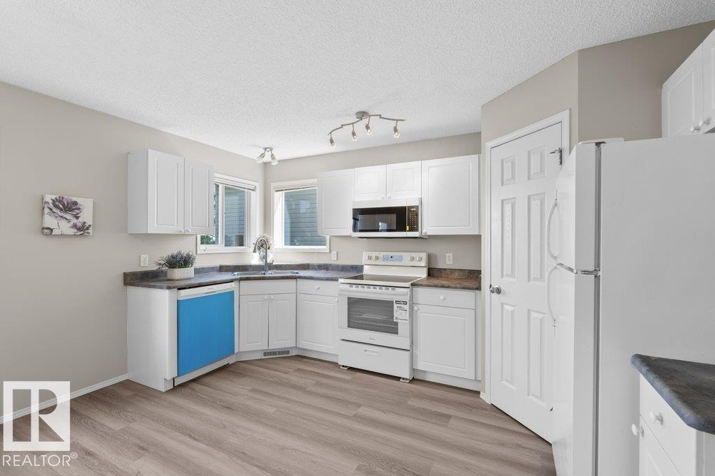 Kitchen featuring white cabinetry, wood-finish flooring, a stainless steel sink, and a built-in microwave - 21344 88 Avenue, Edmonton, AB - Indoor Photo Showing Kitchen