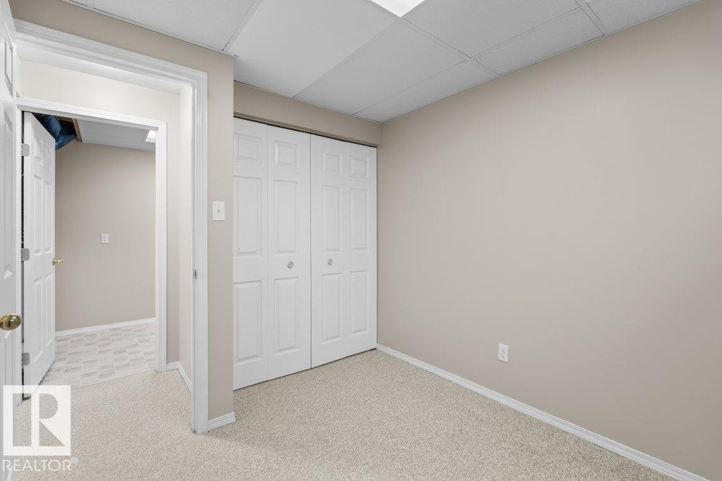 Room featuring light beige wall paint, white bi-fold closet doors, cream-toned carpet flooring, and a white drop ceiling with recessed lighting - 21344 88 Avenue, Edmonton, AB - Indoor Photo Showing Other Room