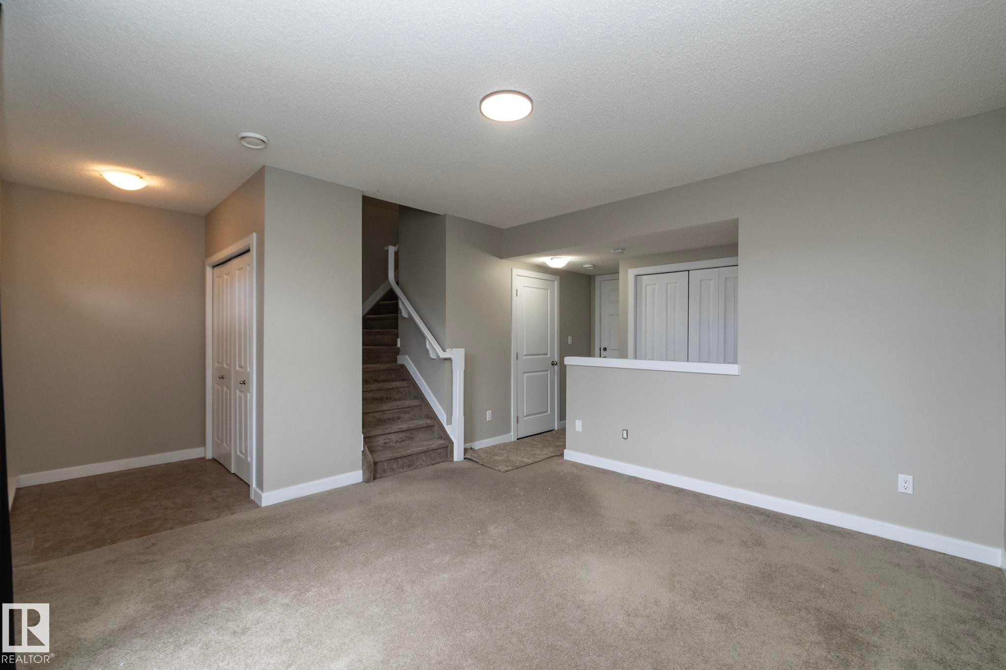 Carpeted living area featuring light neutral wall paint, white baseboards, and a partial wall dividing spaces - 117 Callaghan Drive Sw, Edmonton, AB - Indoor Photo Showing Other Room
