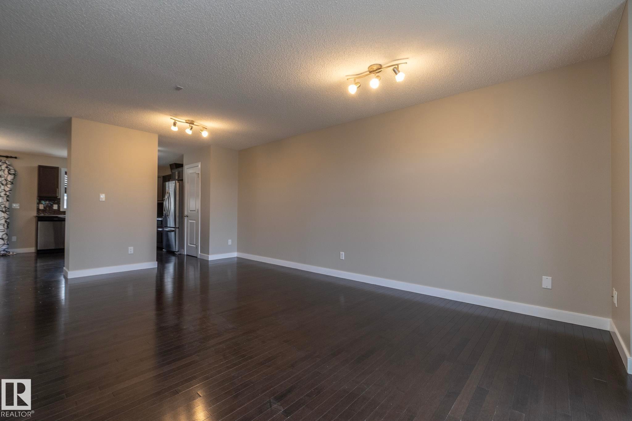 Spacious room featuring dark wood-finish flooring, neutral wall paint, and overhead track lighting - 117 Callaghan Drive Sw, Edmonton, AB - Indoor Photo Showing Other Room