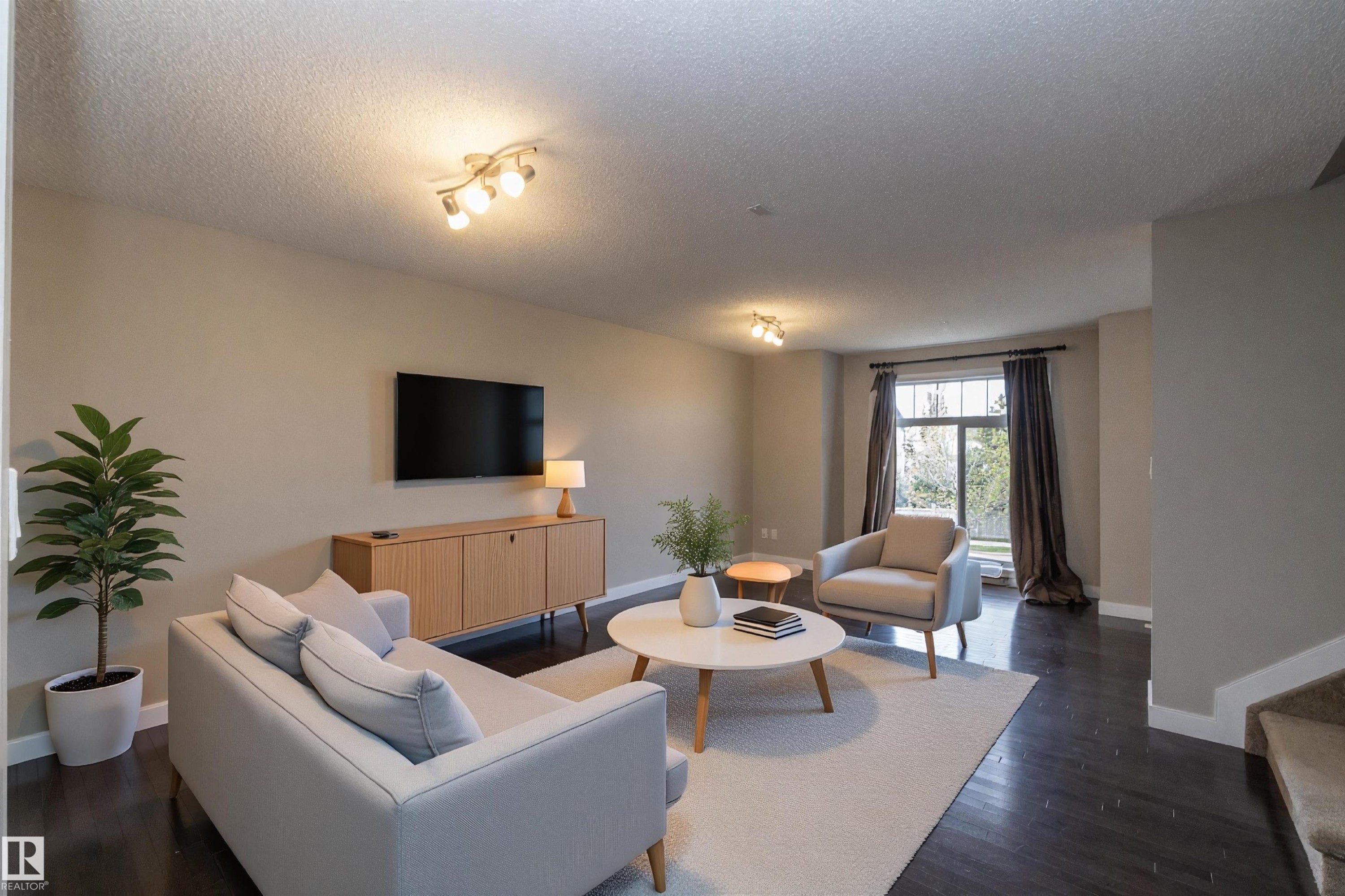 Living area featuring dark wood-finish flooring, a contemporary light fixture, and a large window with privacy coverings - 117 Callaghan Drive Sw, Edmonton, AB - Indoor Photo Showing Living Room