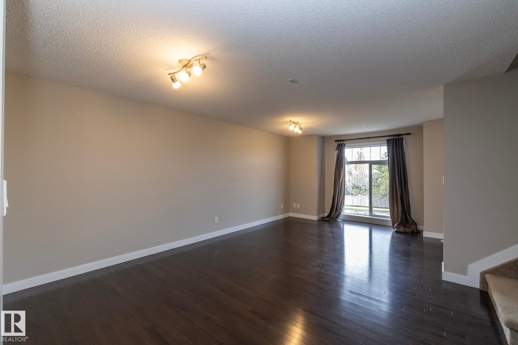 Spacious living area featuring dark wood-finish flooring, neutral wall tones, and white baseboards - 117 Callaghan Drive Sw, Edmonton, AB - Indoor Photo Showing Other Room