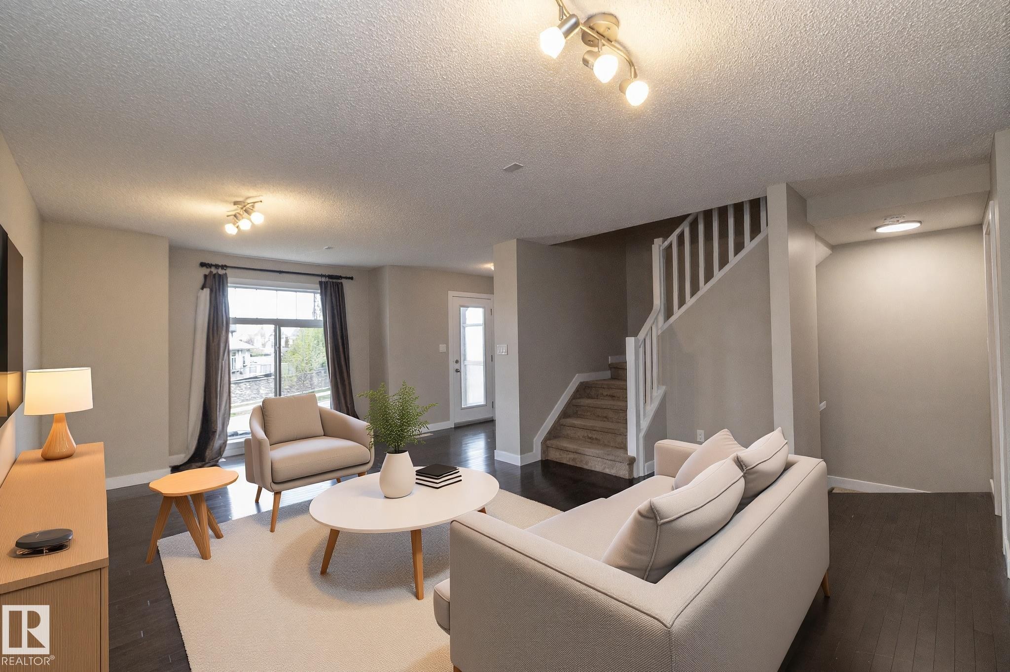 Spacious living area featuring dark wood-finish flooring, a contemporary staircase with white balusters, light gray wall paint, and recessed lighting fixtures - 117 Callaghan Drive Sw, Edmonton, AB - Indoor Photo Showing Living Room