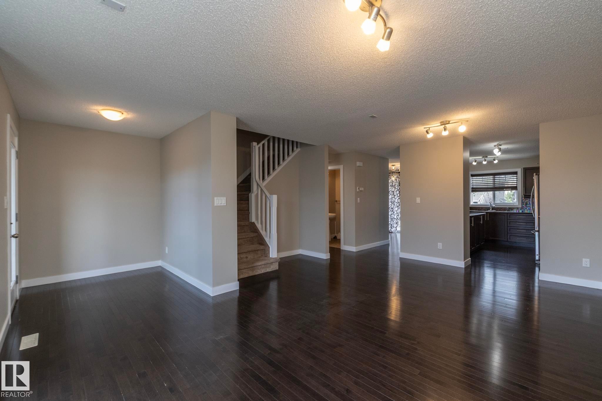 Spacious interior featuring dark wood-finish flooring, light neutral-toned walls, and white trim throughout - 117 Callaghan Drive Sw, Edmonton, AB - Indoor Photo Showing Other Room