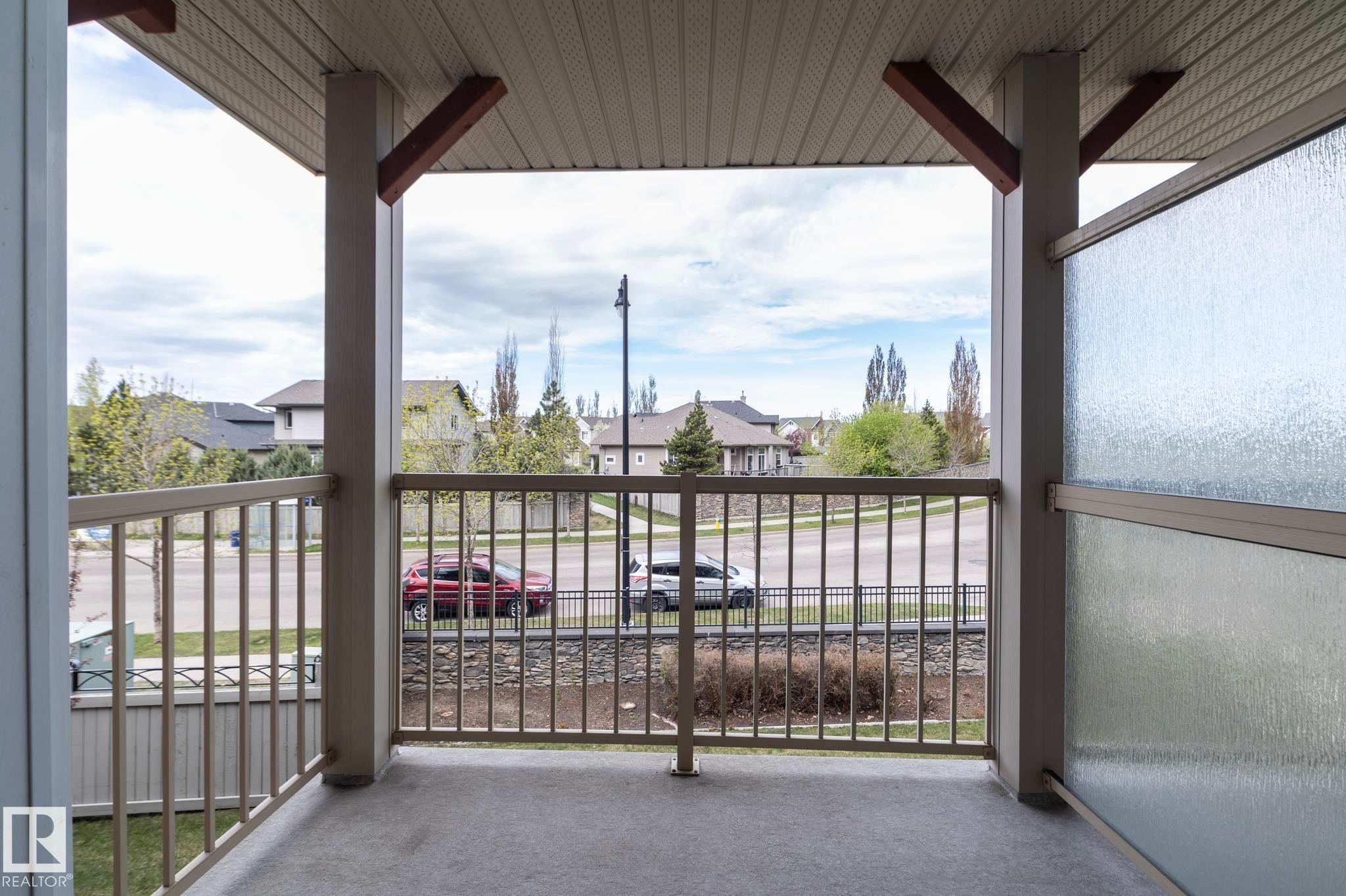 Covered outdoor balcony featuring a textured concrete floor, light-toned metal railing, and a privacy panel with textured glass - 117 Callaghan Drive Sw, Edmonton, AB - Outdoor With Exterior