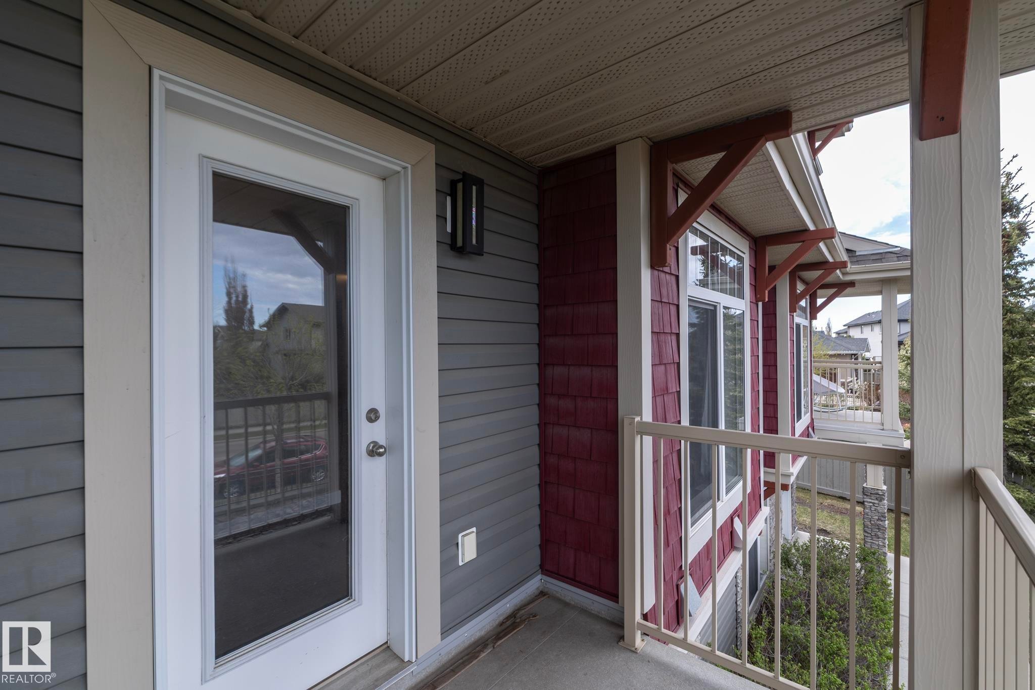 Private exterior balcony featuring a white glass-paneled door, gray horizontal siding, red shake siding, white window trim, and a cream-colored railing - 117 Callaghan Drive Sw, Edmonton, AB - Outdoor With Exterior