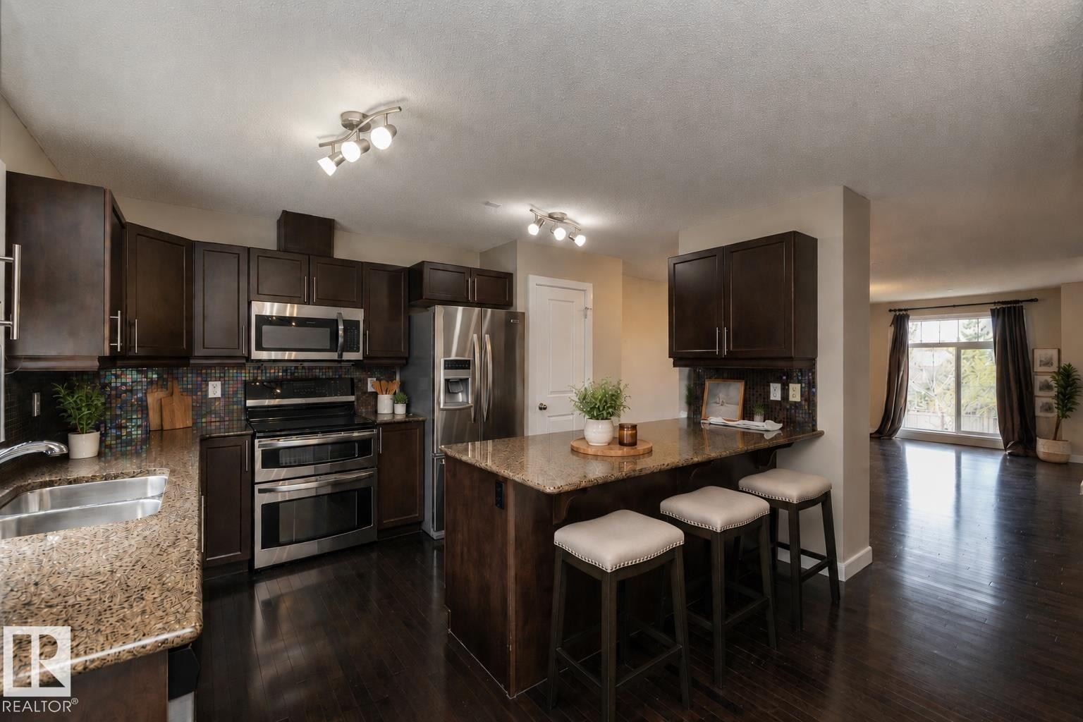 Kitchen featuring dark wood-finish cabinetry, stainless steel appliances, speckled stone countertops, and a patterned backsplash - 117 Callaghan Drive Sw, Edmonton, AB - Indoor Photo Showing Kitchen With Double Sink With Upgraded Kitchen