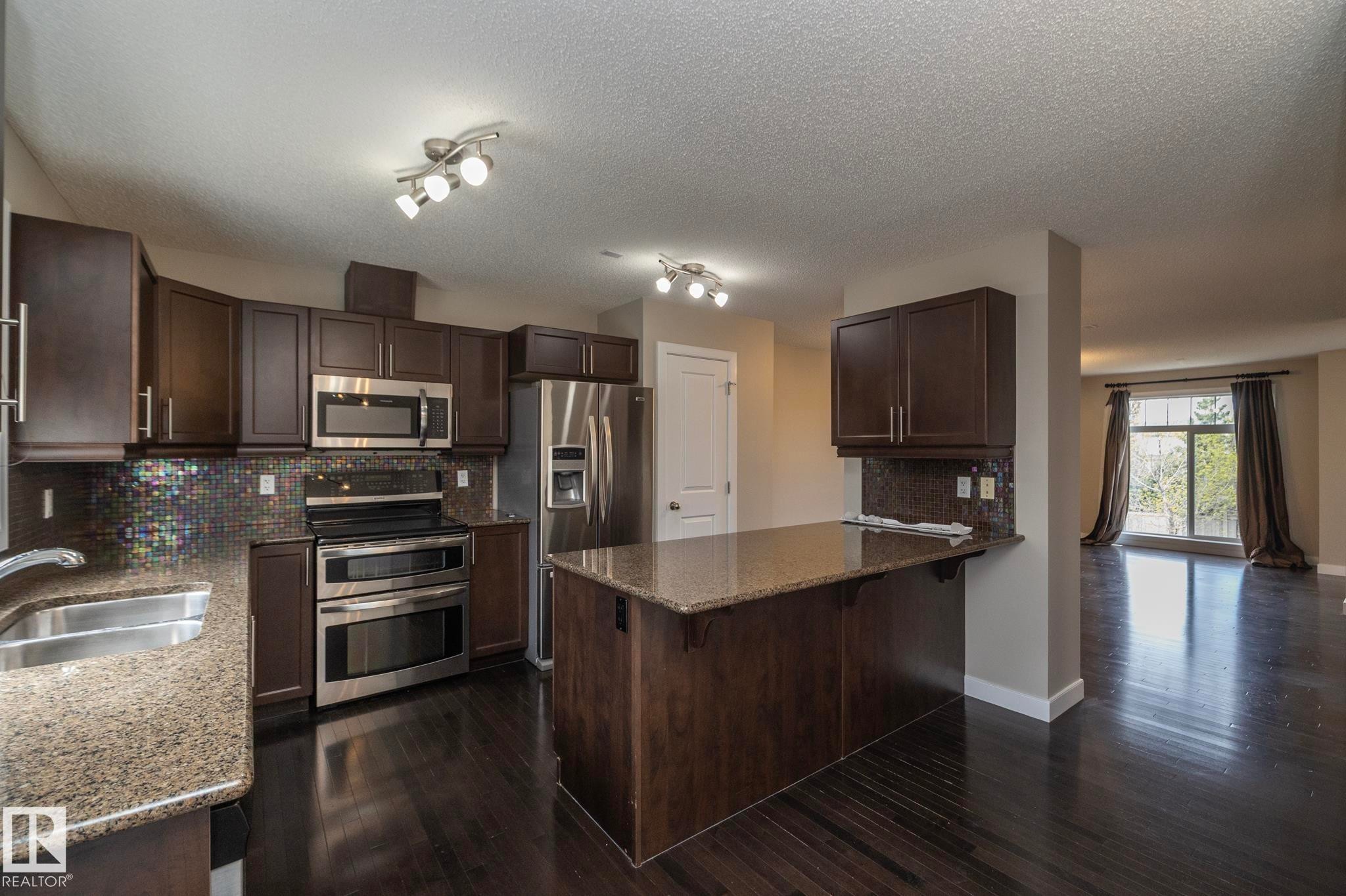 Kitchen featuring dark wood-finish cabinetry and a complementary island with a breakfast bar - 117 Callaghan Drive Sw, Edmonton, AB - Indoor Photo Showing Kitchen With Double Sink With Upgraded Kitchen