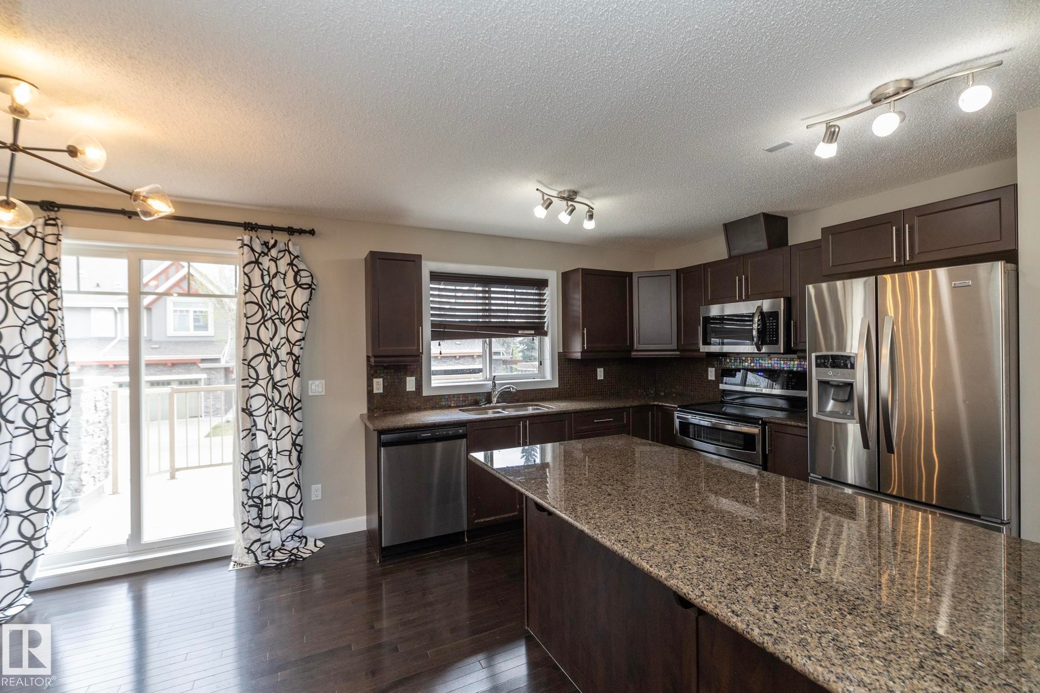 Kitchen featuring dark wood-finish cabinetry, stainless steel appliances, and granite countertops - 117 Callaghan Drive Sw, Edmonton, AB - Indoor Photo Showing Kitchen