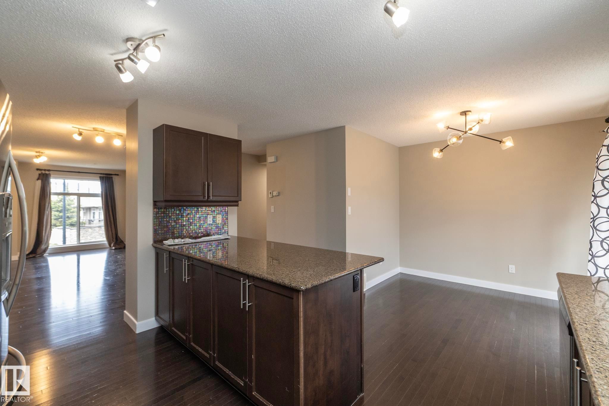 Open-concept living area featuring dark wood-finish flooring, a kitchen island with a stone-finish countertop, and a mosaic tile backsplash - 117 Callaghan Drive Sw, Edmonton, AB - Indoor Photo Showing Kitchen