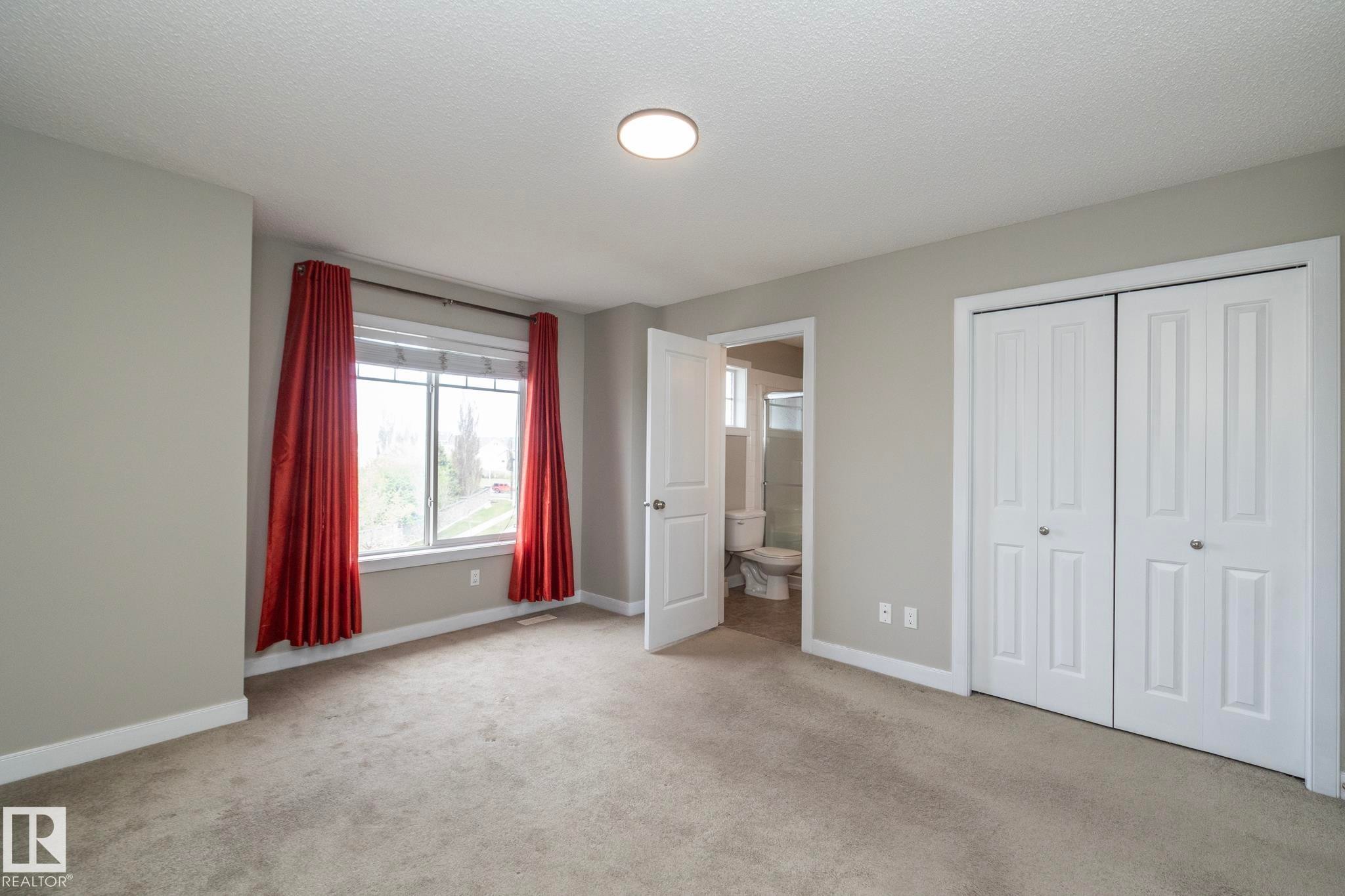 Carpeted room featuring a double window, overhead flush-mount lighting, bi-fold closet doors, and light grey wall paint with white baseboards - 117 Callaghan Drive Sw, Edmonton, AB - Indoor