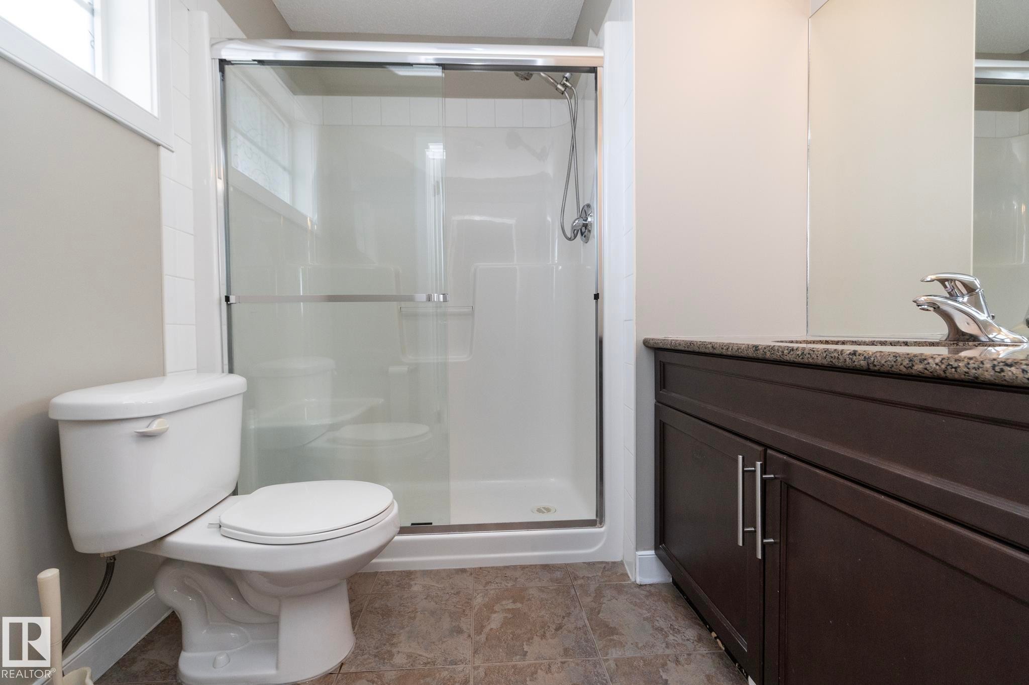 Bathroom featuring a glass-enclosed shower, dark wood-finish vanity with a stone countertop, chrome fixtures, and neutral wall tones - 117 Callaghan Drive Sw, Edmonton, AB - Indoor Photo Showing Bathroom